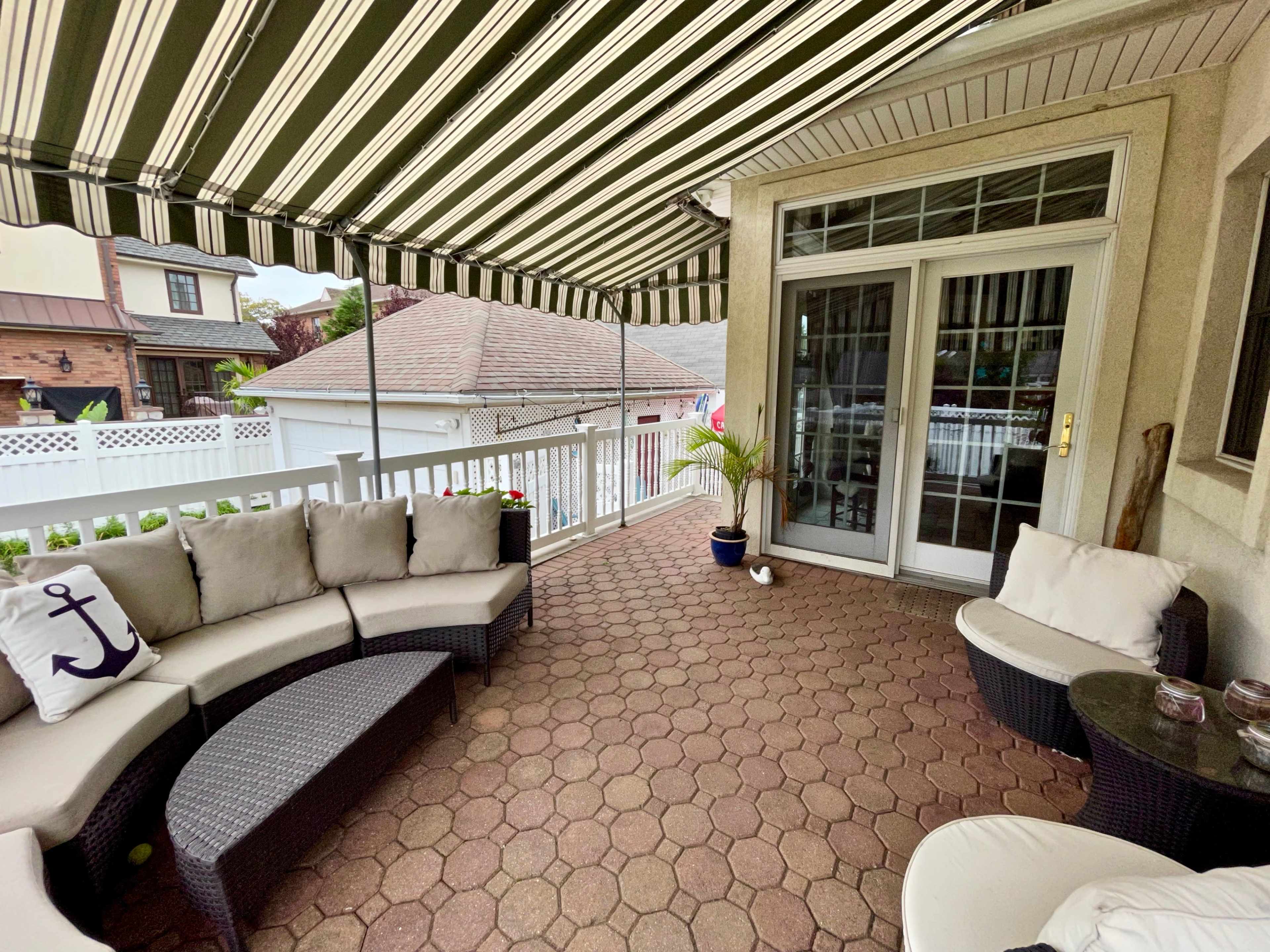 A patio with a striped awning, featuring a curved sectional couch, a small table, and a potted plant.
