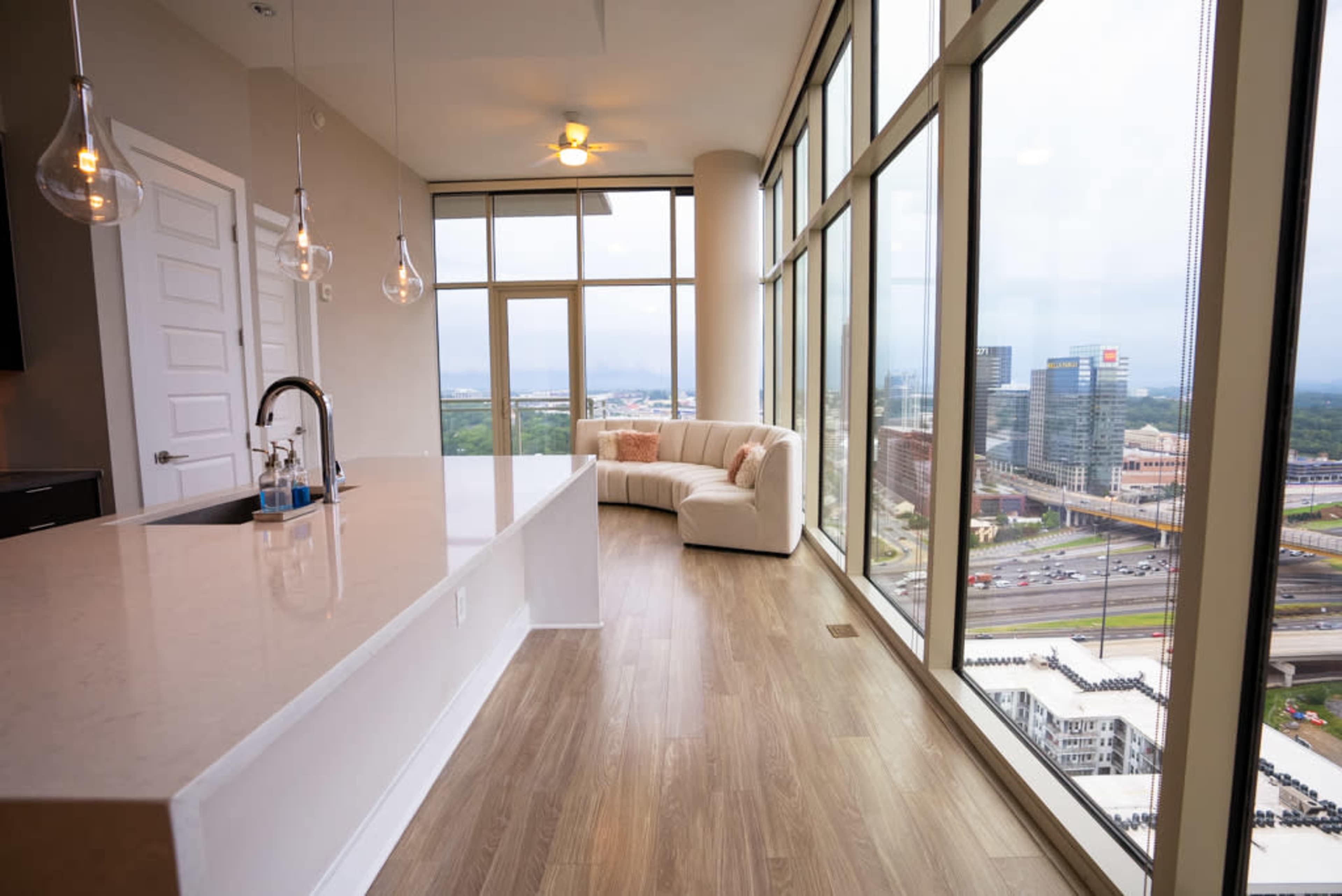 A modern apartment features a spacious kitchen area with a large island and floor-to-ceiling windows offering a view of the city skyline.