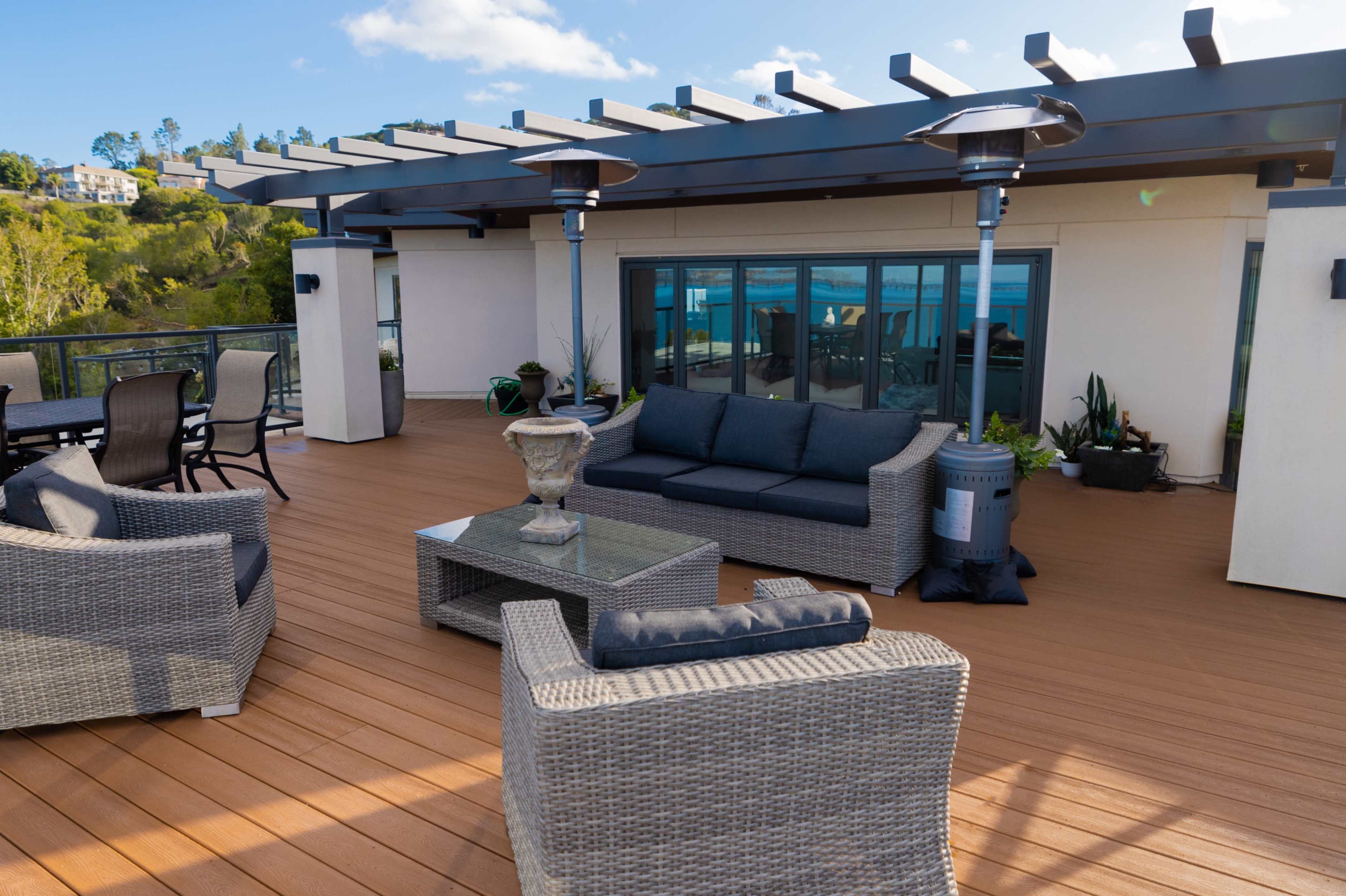 A modern rooftop terrace features a seating area with wicker furniture, a glass table, and patio heaters.