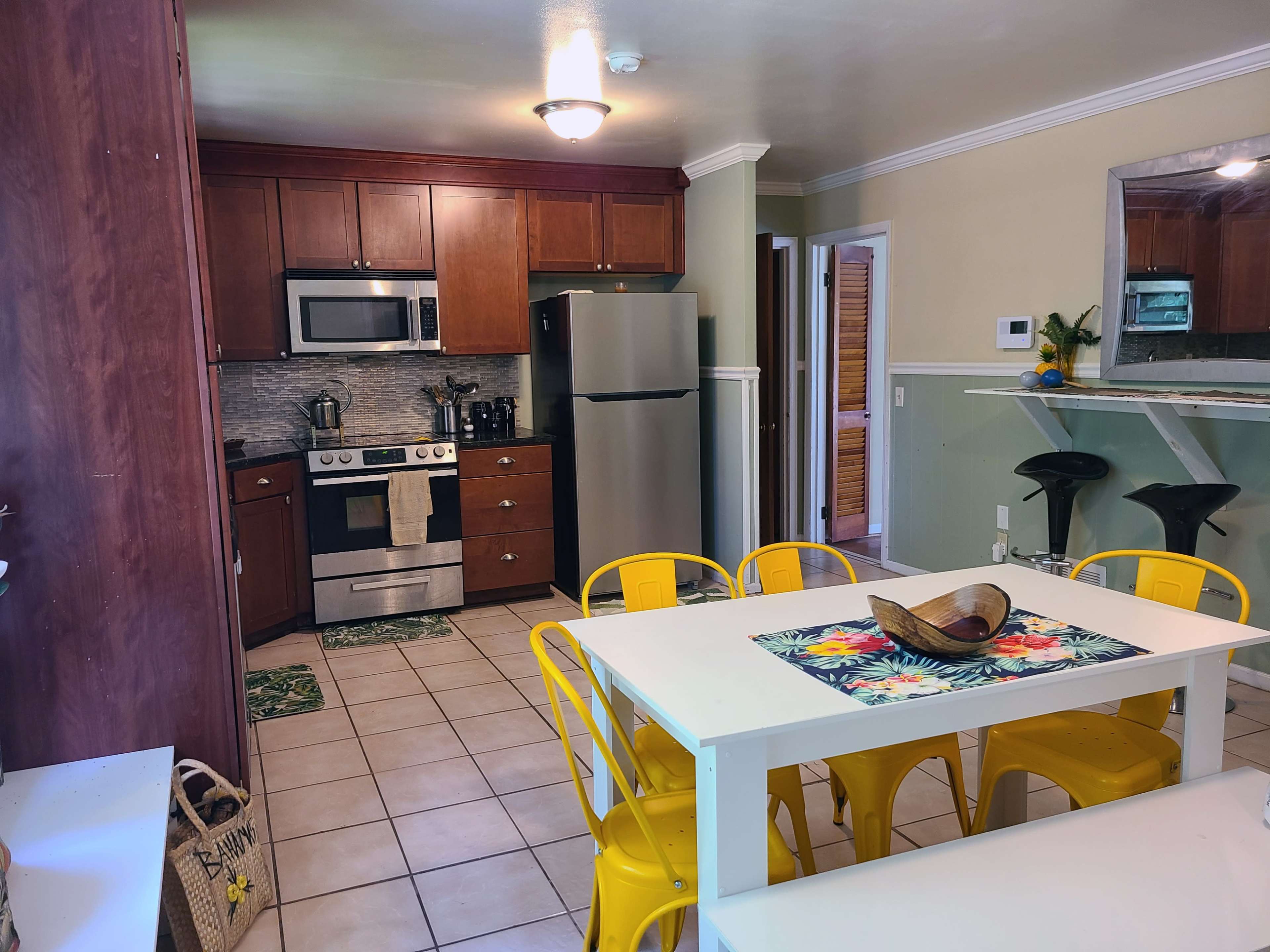 A kitchen with modern appliances, wooden cabinets, and a dining table surrounded by yellow chairs.