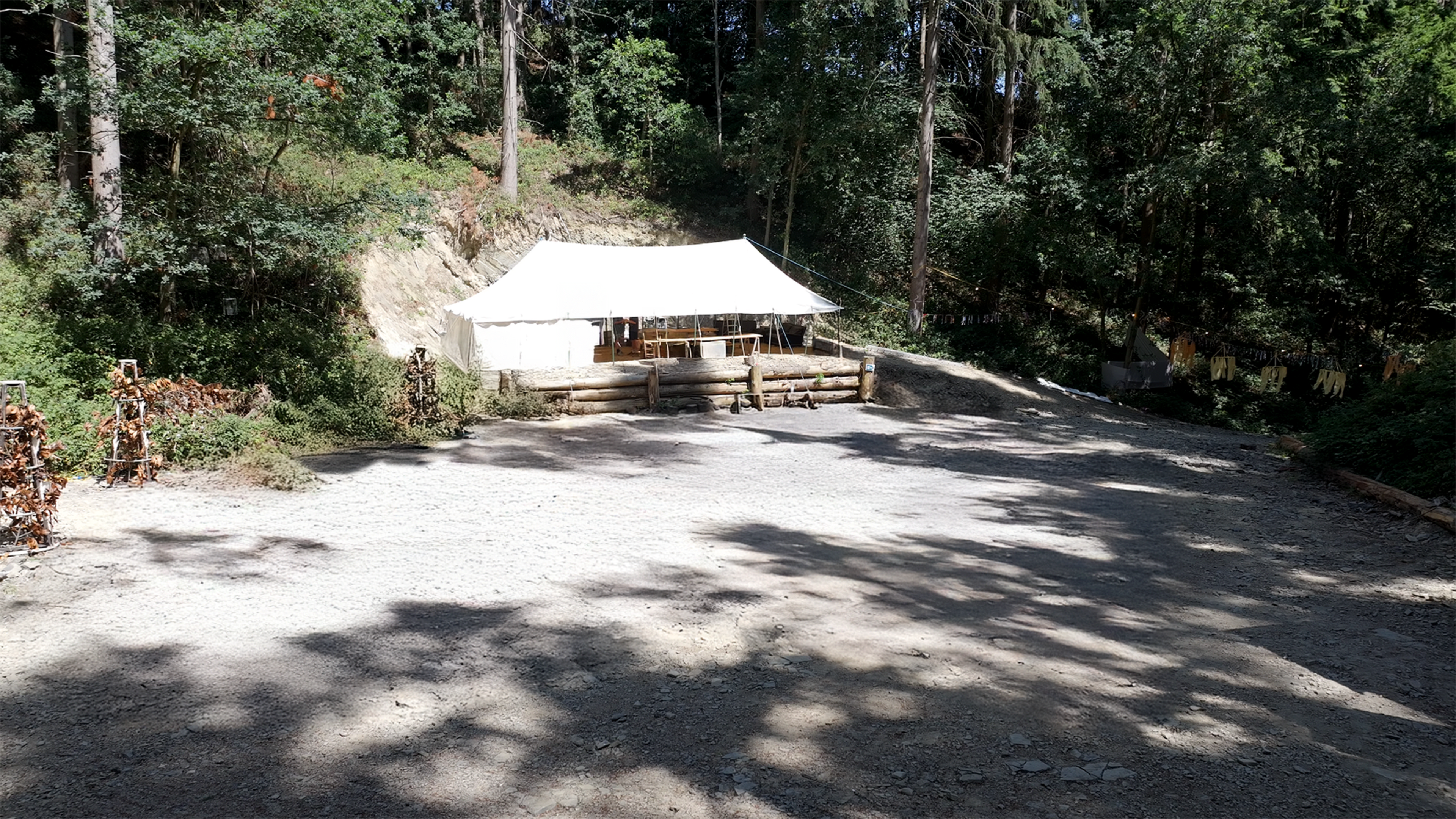 A white tent is set up on a gravel clearing surrounded by trees.