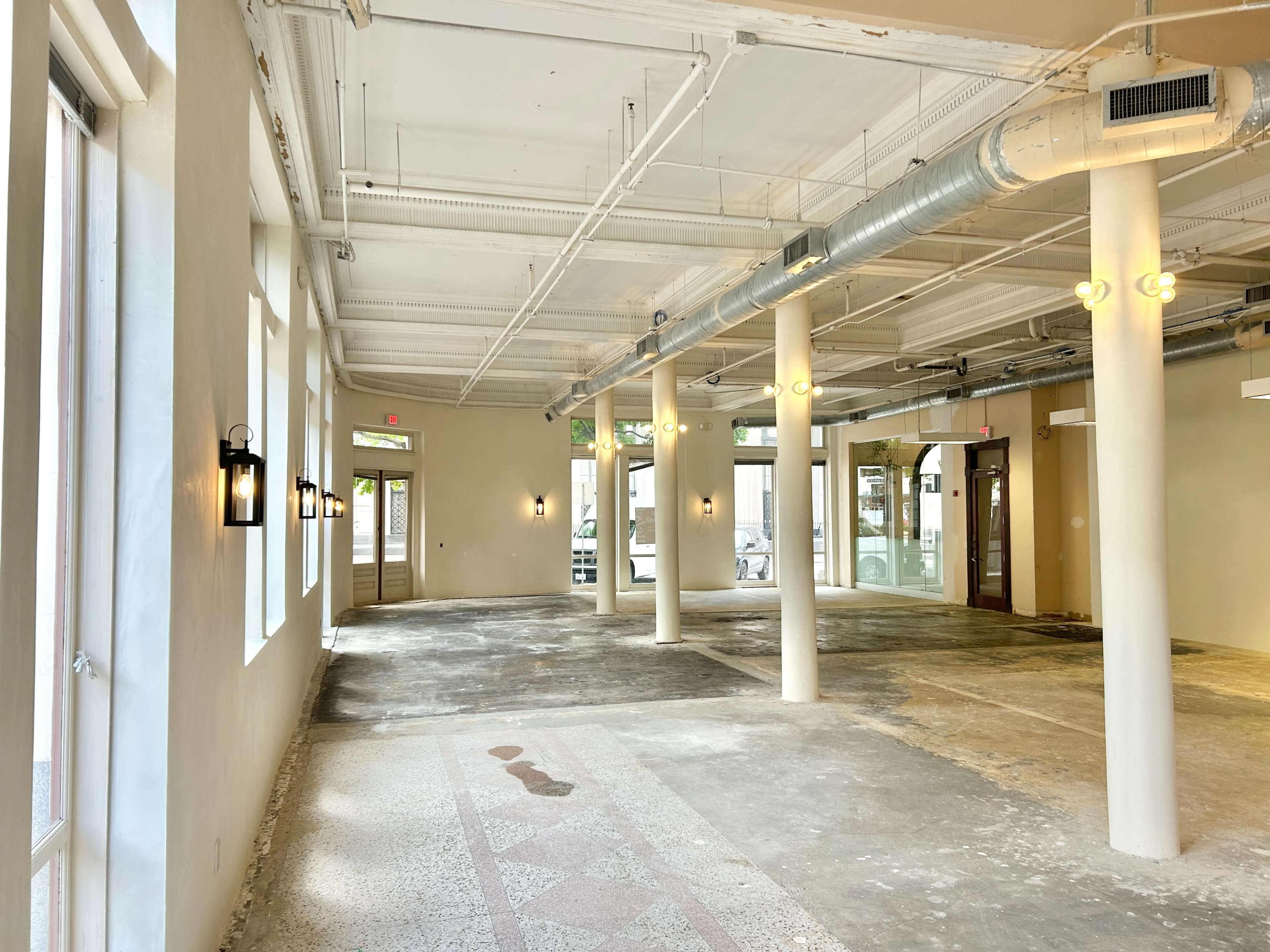 The image shows an empty interior space with concrete flooring, white walls, and several light fixtures mounted on the walls.