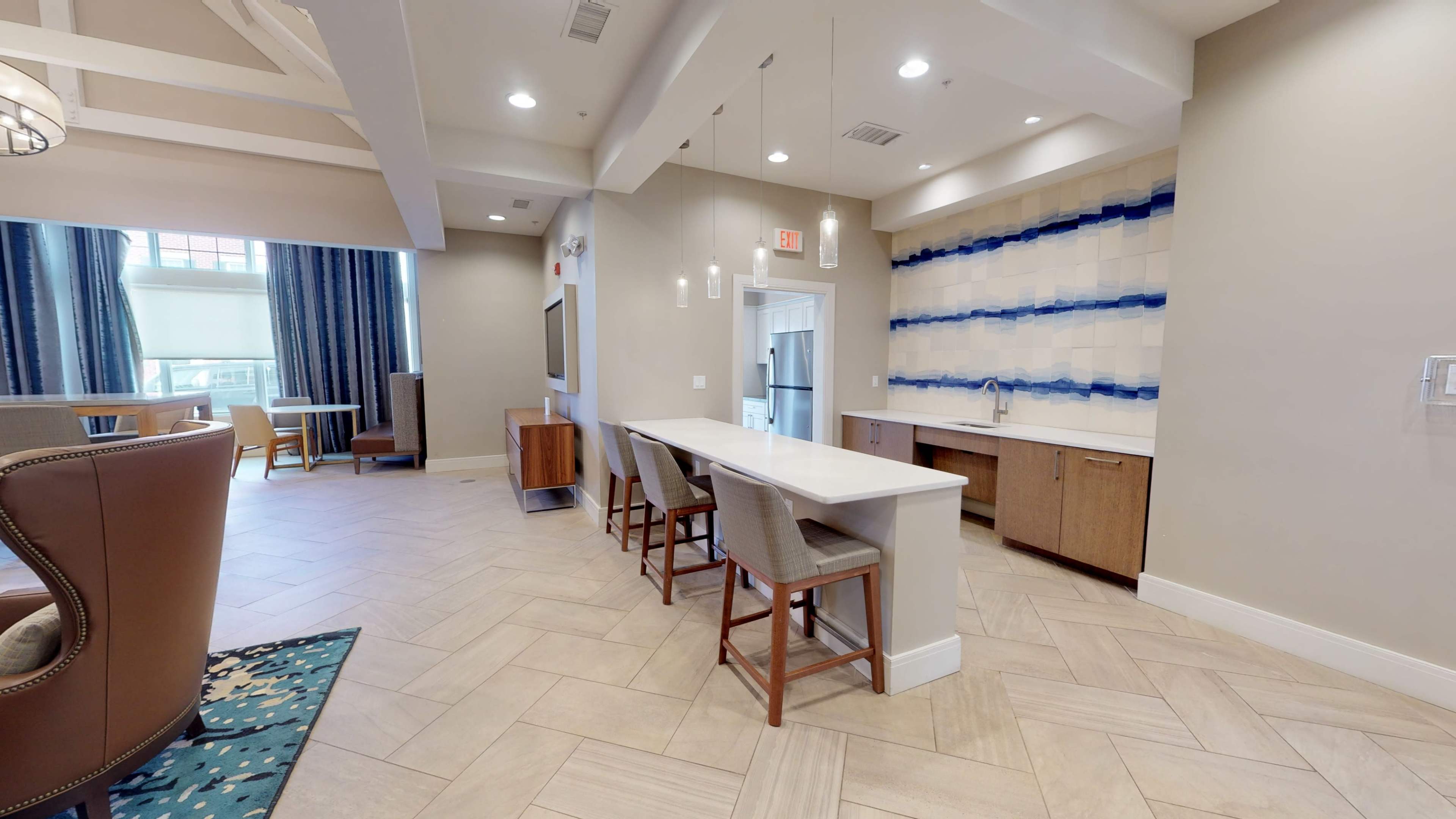 A modern interior space featuring a seating area, a kitchen counter with stools, and decorative wall paneling.