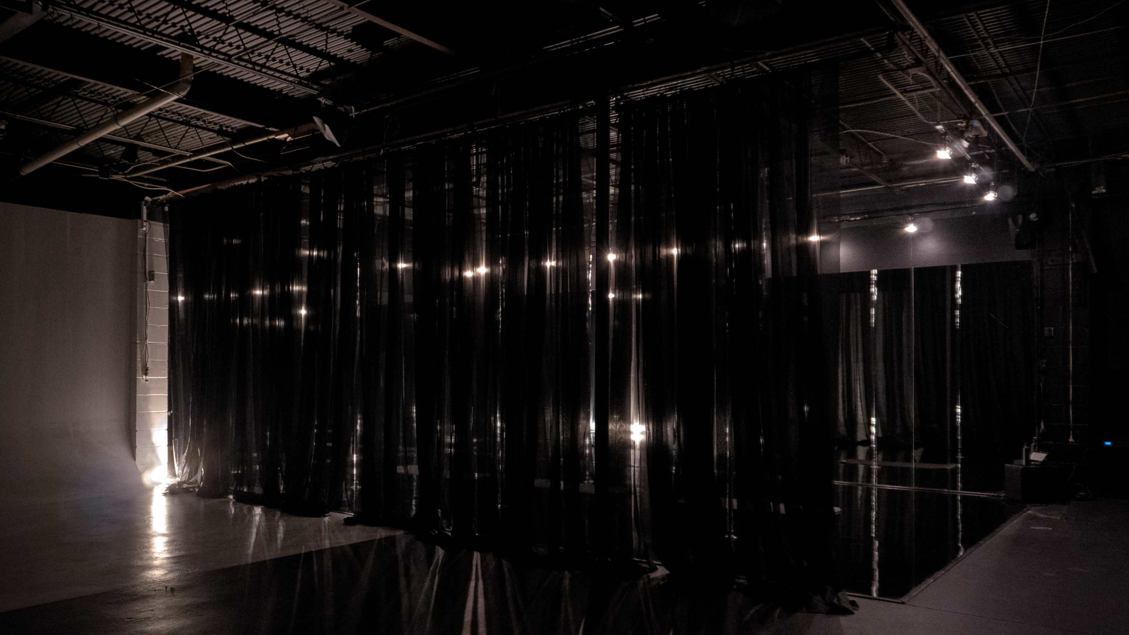 The image shows a dimly lit space with black sheer curtains hanging, creating an atmosphere of separation within the room.