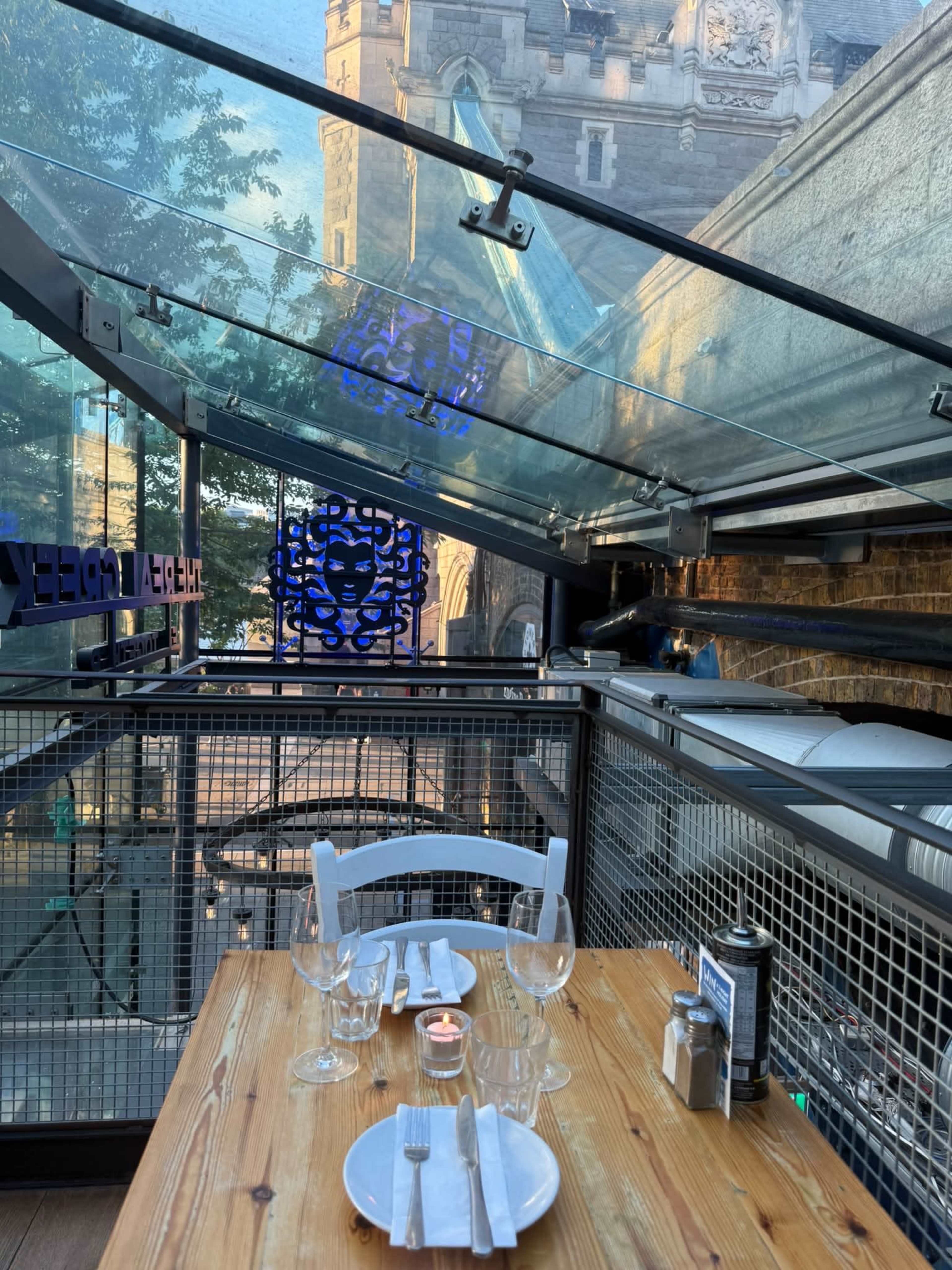 A dining table is set for a meal on a patio with a glass roof, overlooking an urban street.
