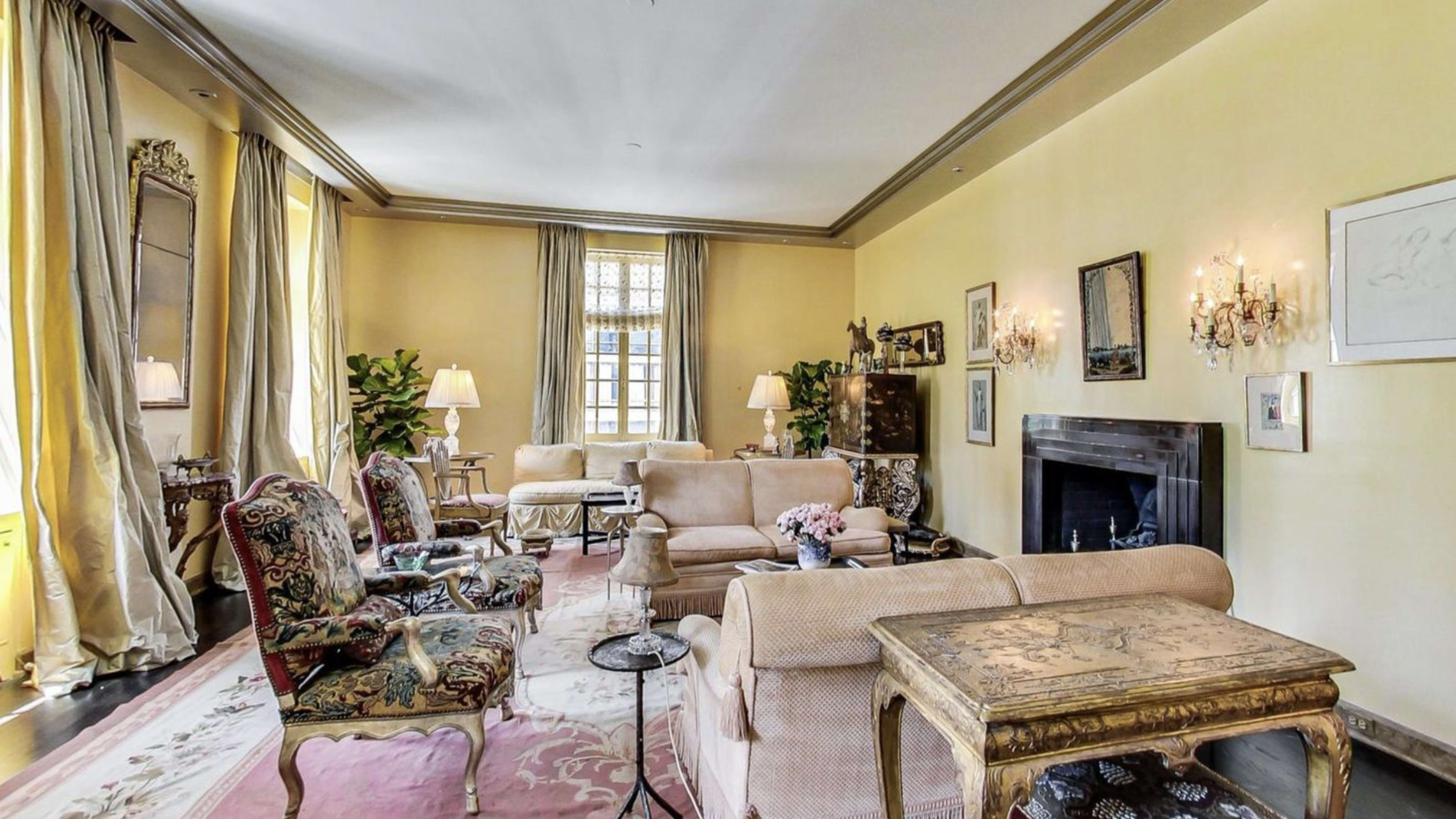 A living room with light yellow walls, a fireplace, and antique furniture arranged around a central area rug.