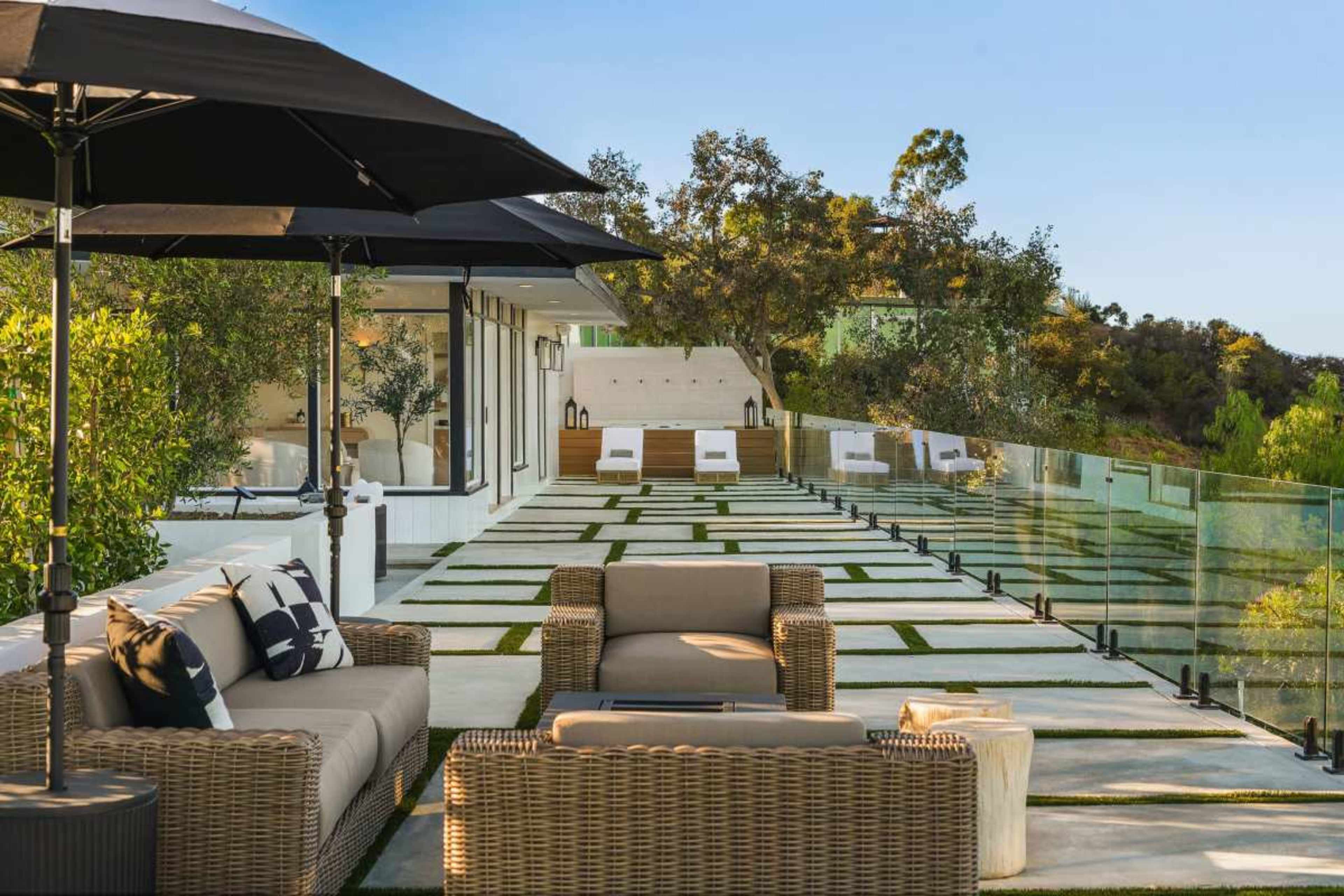 A spacious outdoor terrace features modern wicker furniture, a large umbrella, and landscaped pathways bordered by greenery.