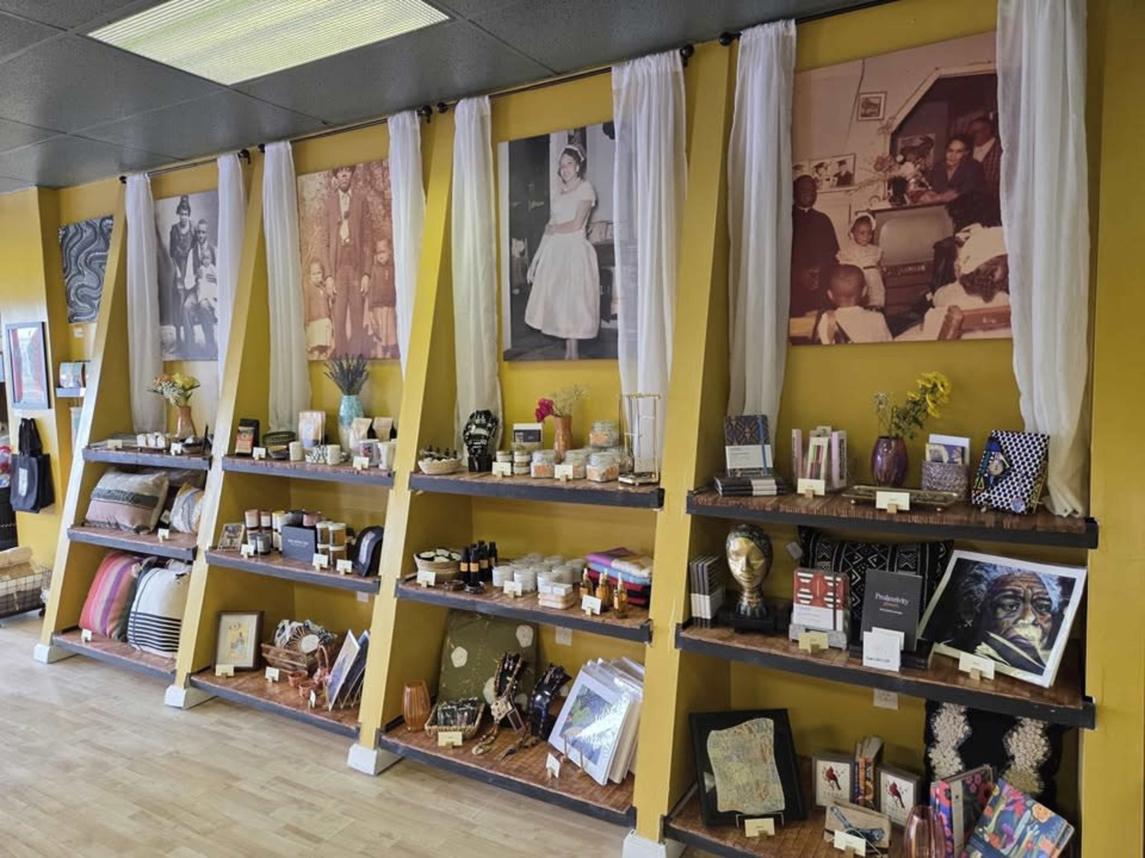 The image shows a retail space with shelves displaying various home goods and decorative items, complemented by historical black-and-white photographs on the yellow wall behind.