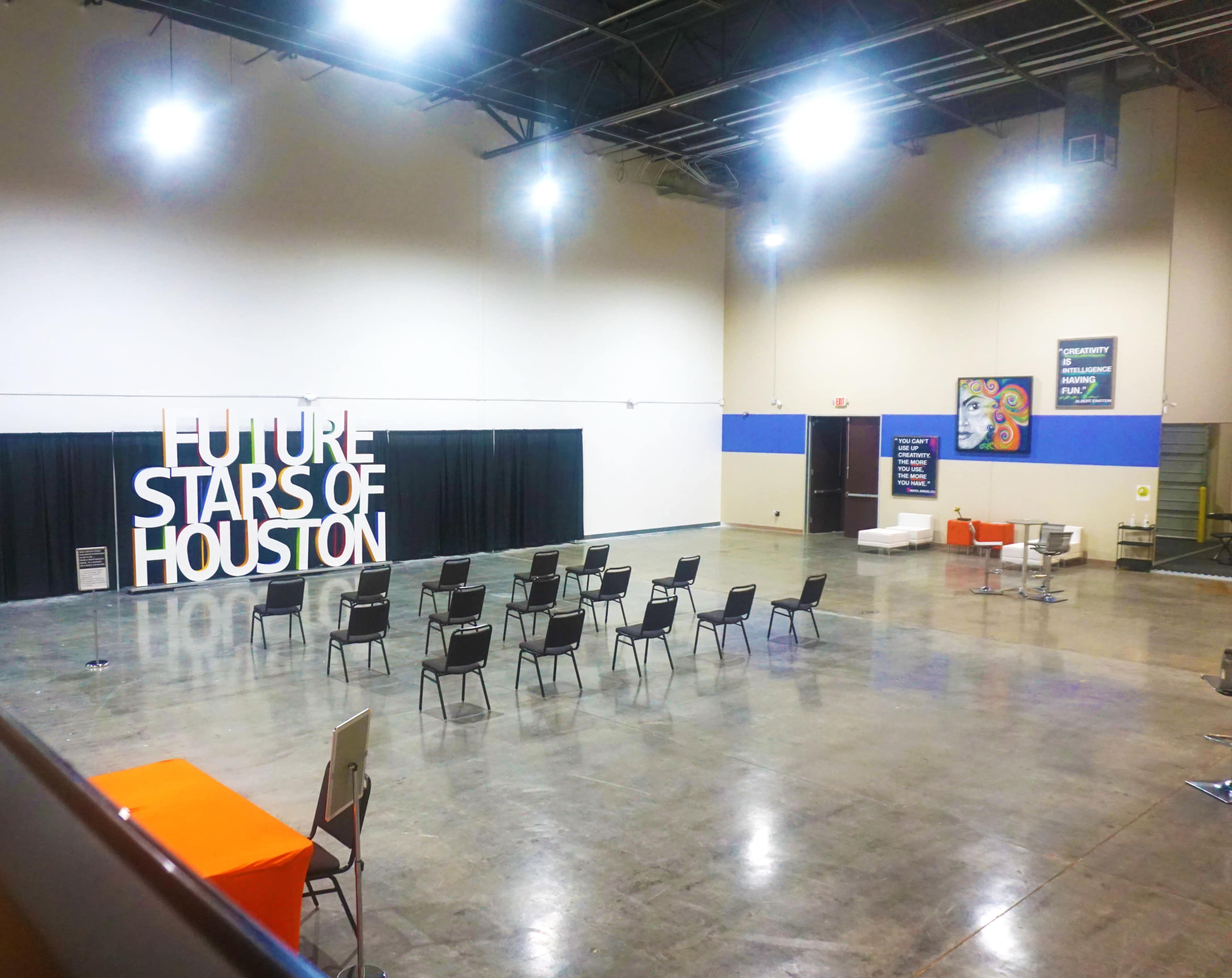 An empty event space set up with black chairs arranged in rows in front of a large white sign that reads "FUTURE STARS OF HOUSTON."