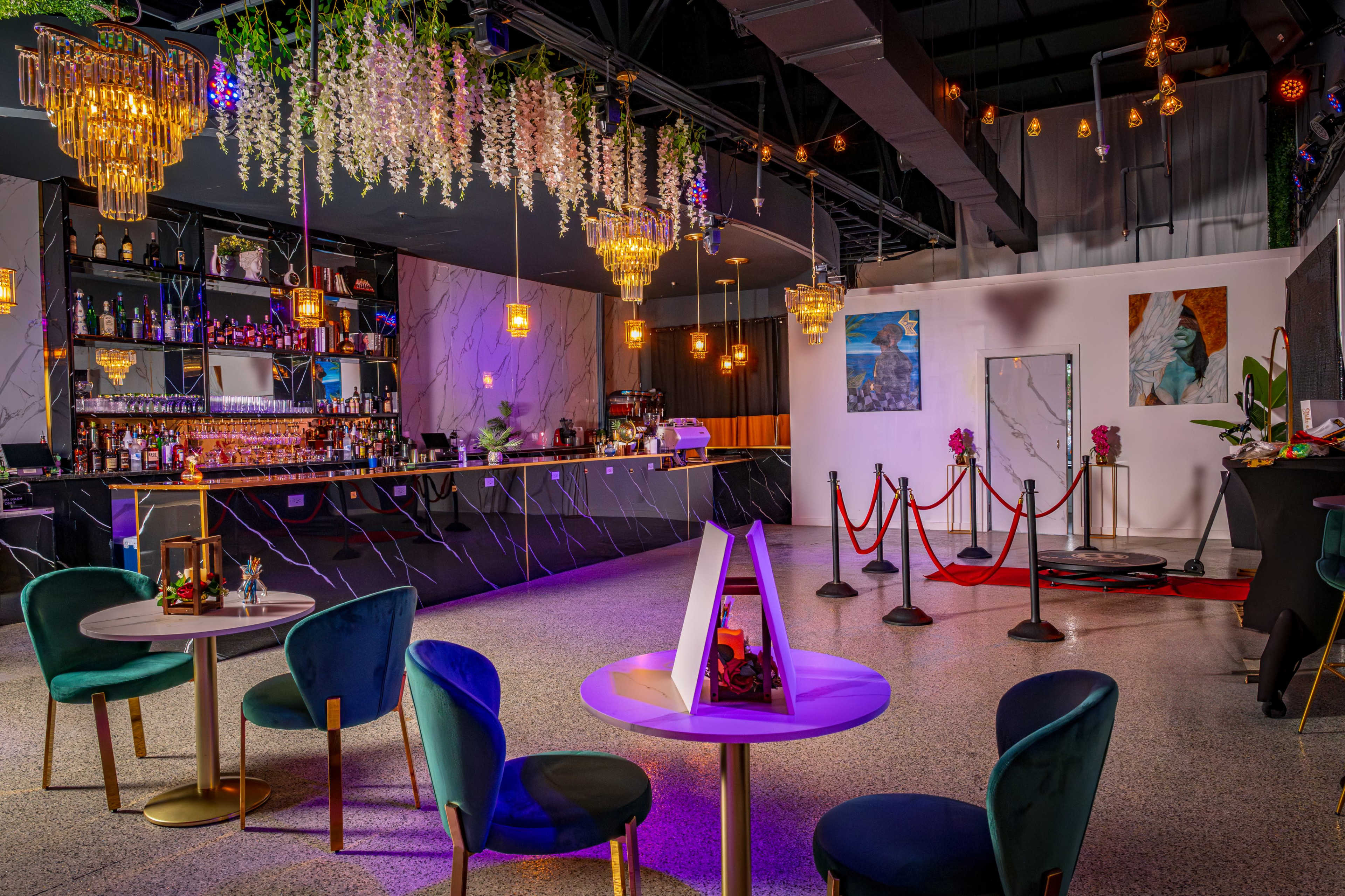 The image shows a stylish bar area with glowing pendant lights, a marble bar counter, seating arrangements, and decorative plants hanging from the ceiling.
