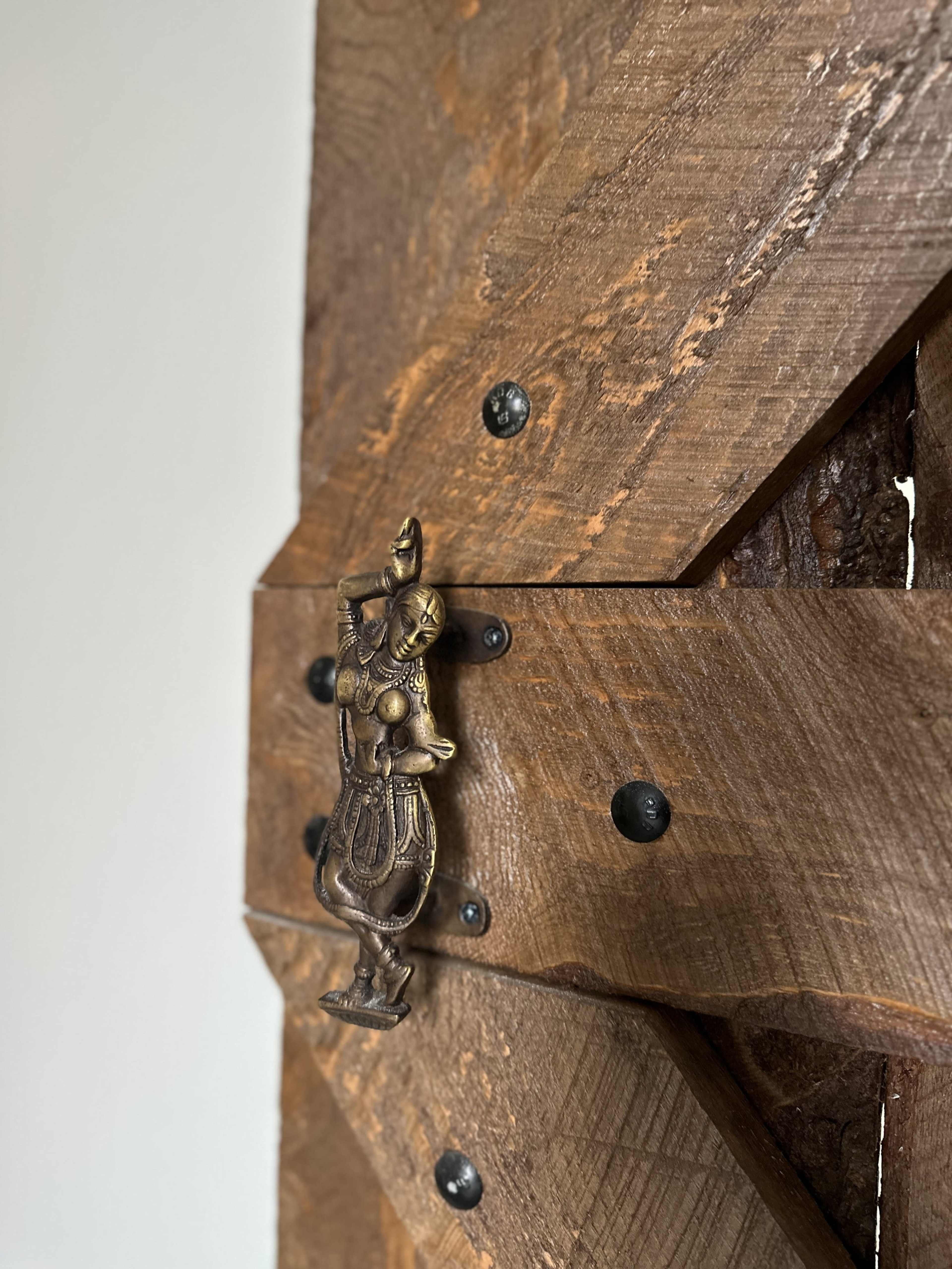 A brass door handle shaped like a dancer is mounted on a wooden door with a rustic design.