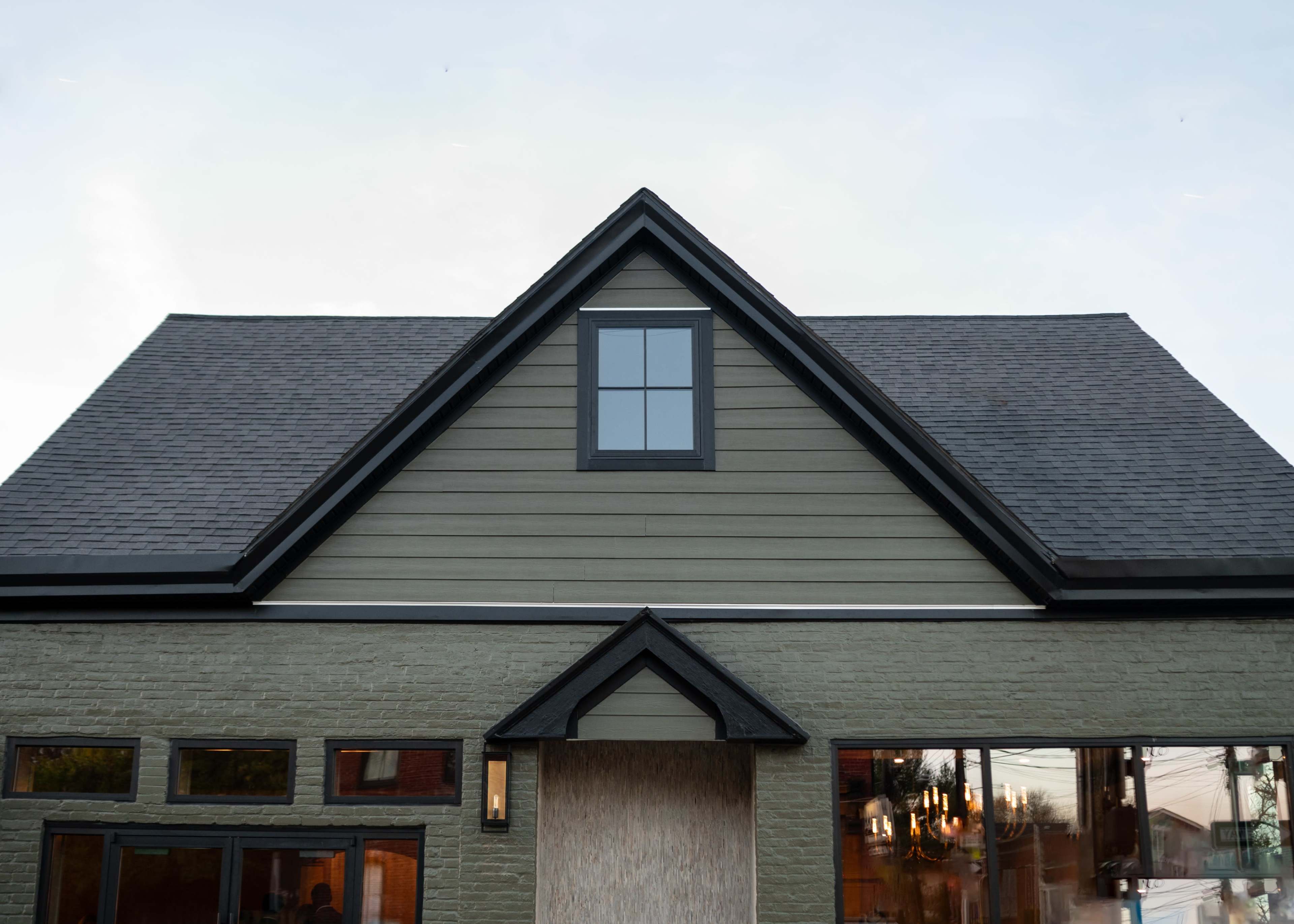 The front of a house featuring a triangular roof with a window and various windows on the lower level.