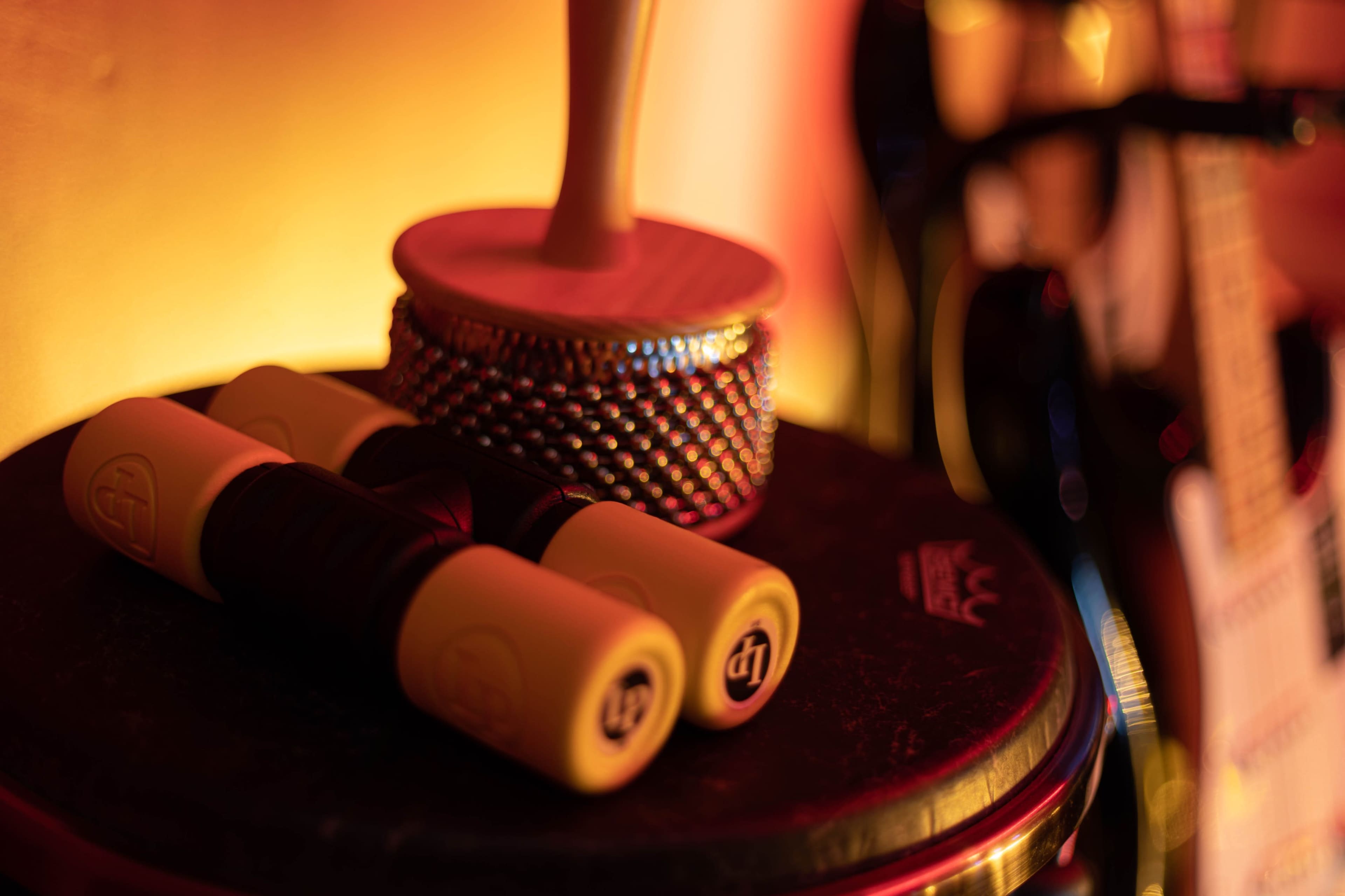A pair of yellow maraca handles rest on a dark surface beside a traditional percussion instrument and a guitar.