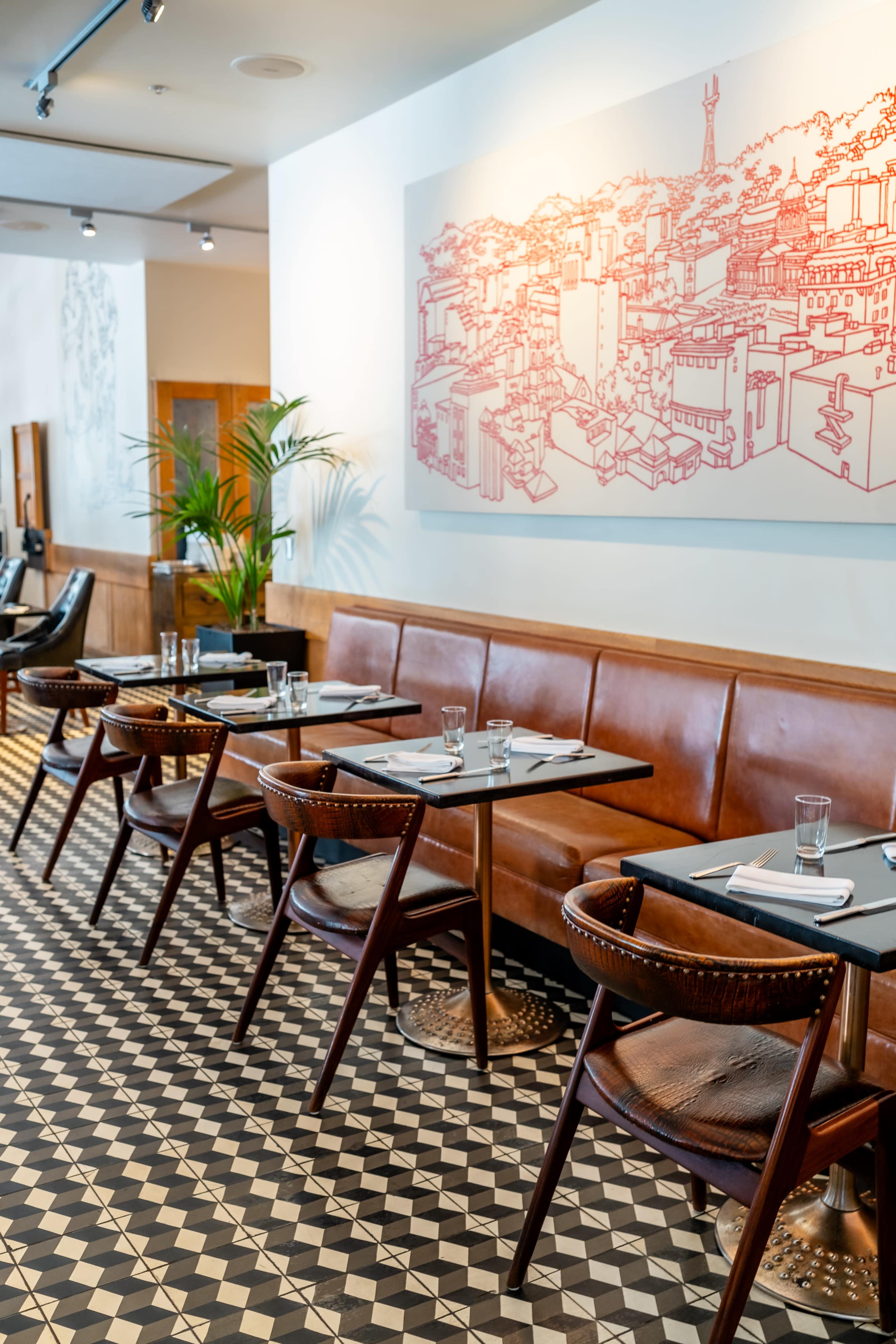 The image shows a modern restaurant interior with brown leather seating, patterned black and white tile flooring, and a large red wall art displaying a cityscape.