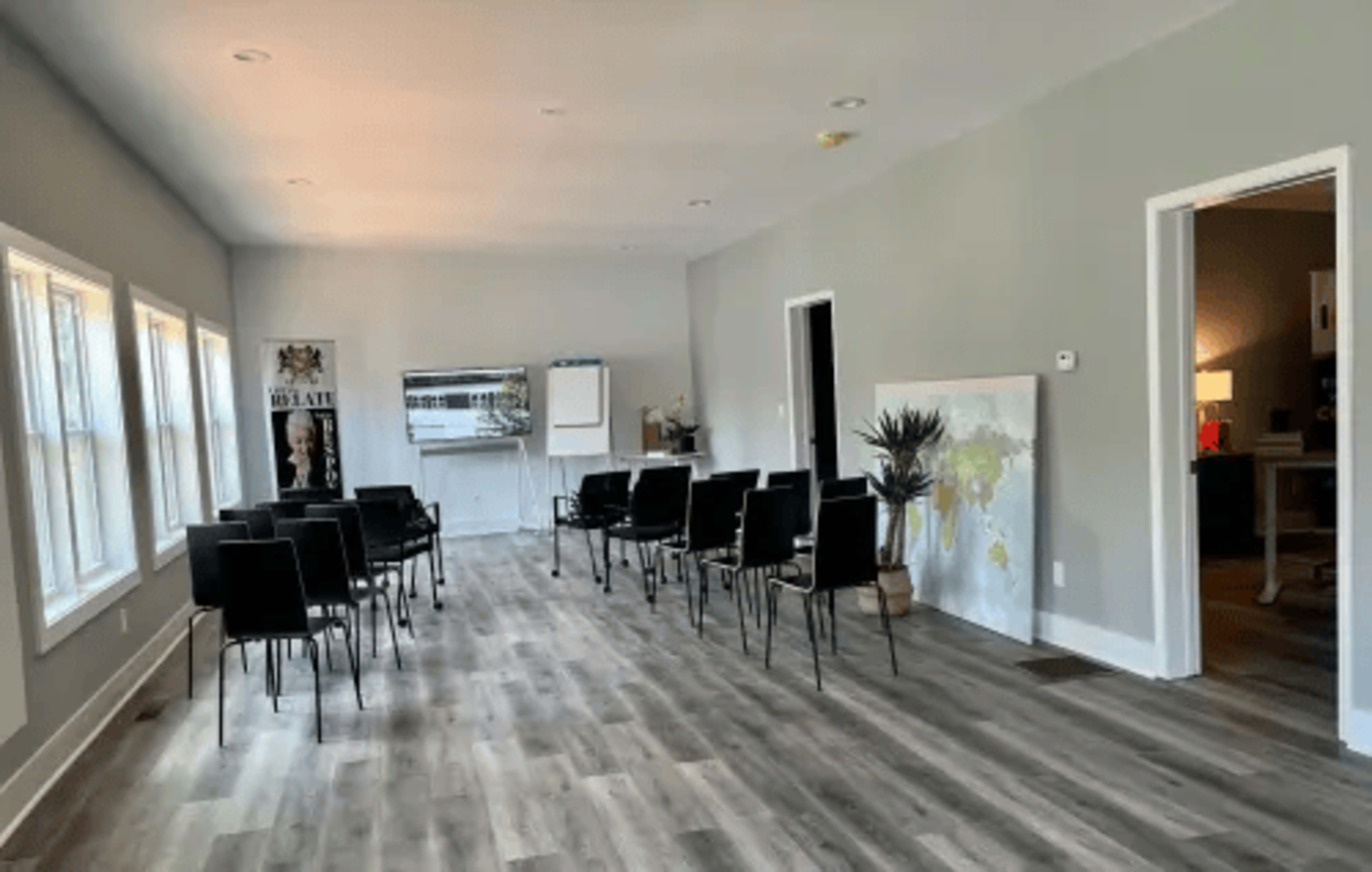 A brightly lit, minimalist room with several black chairs arranged in rows and a large artwork on the wall.