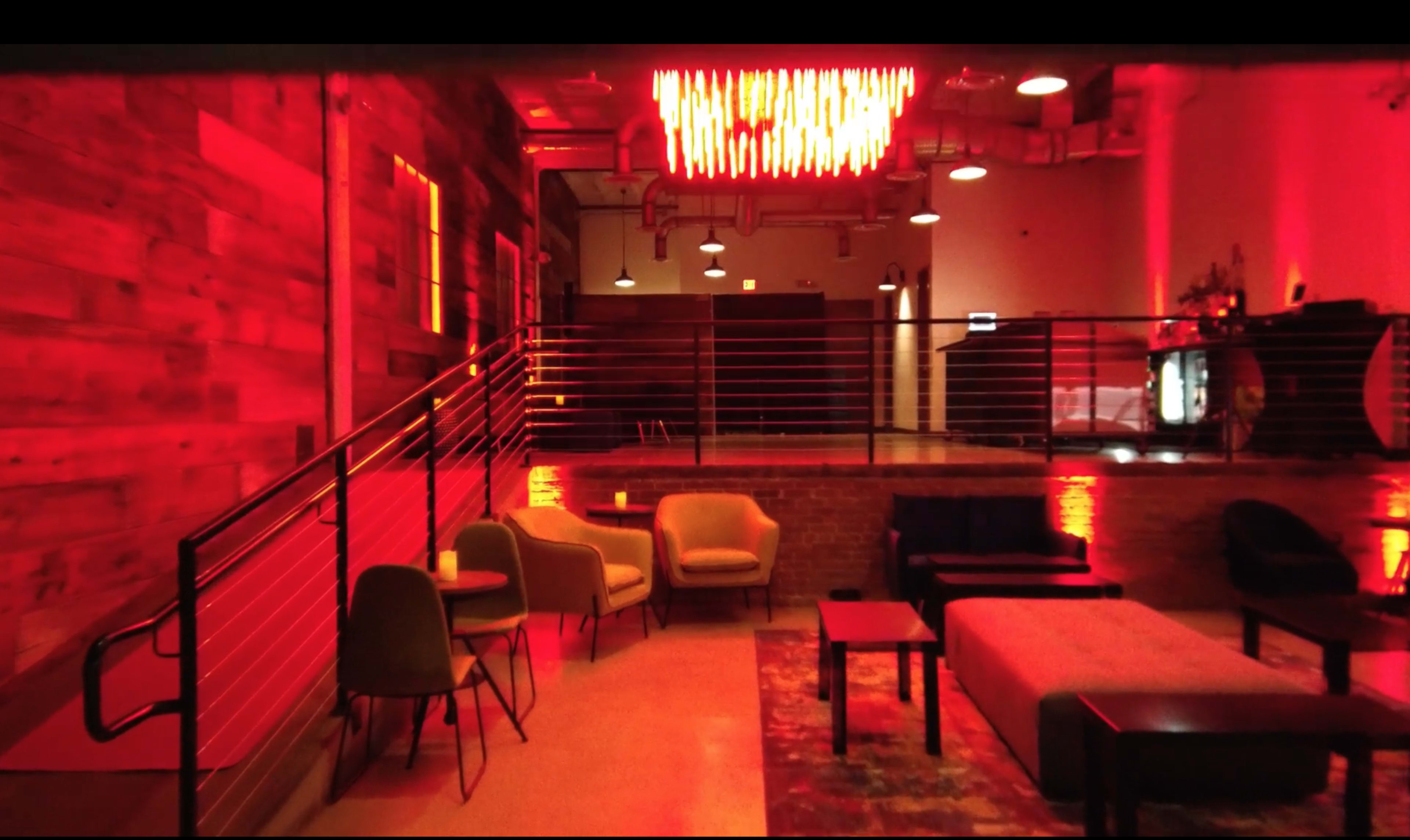 The scene shows a modern lounge area with a mix of seating, wooden walls, and red lighting fixtures overhead.
