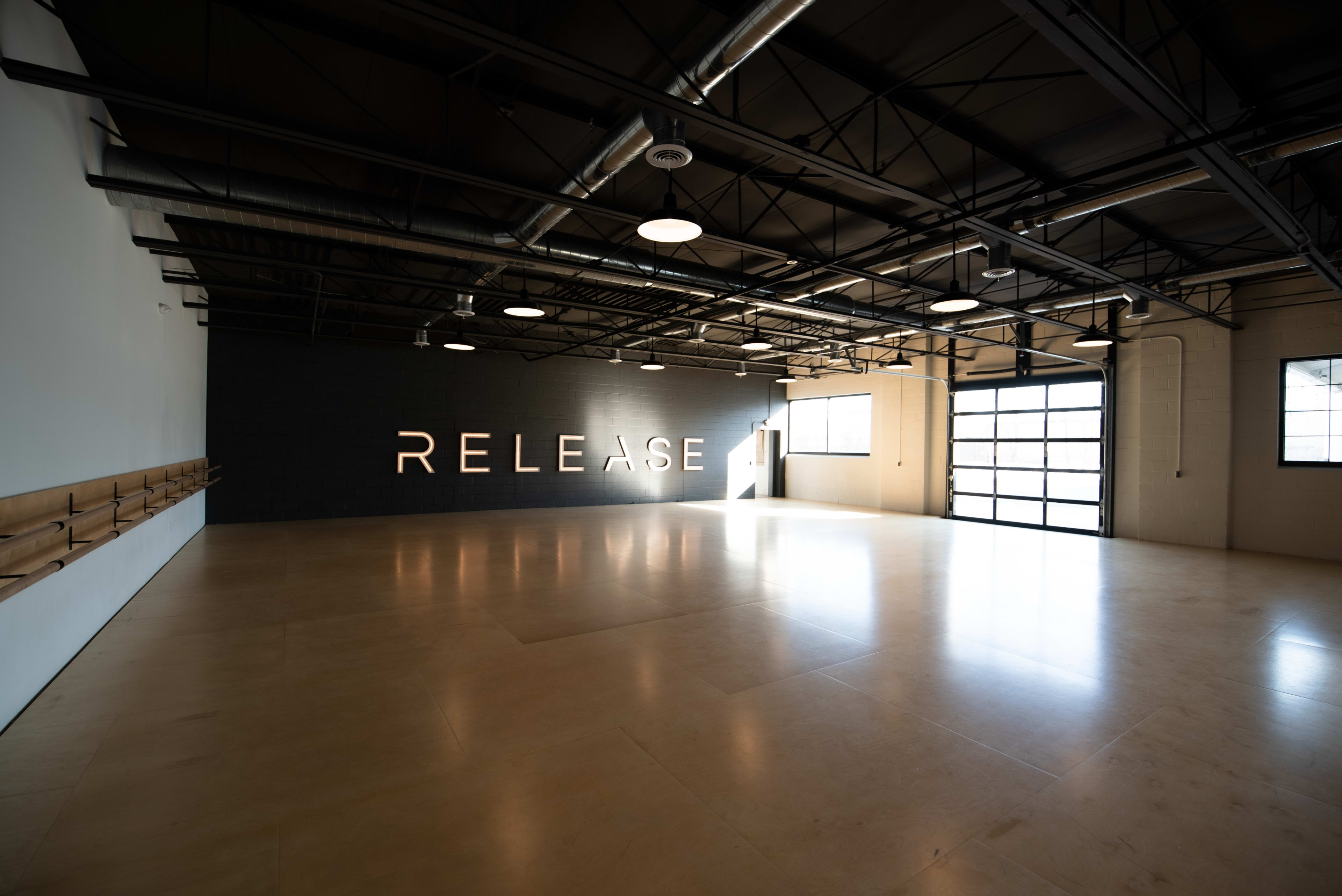 The image shows a spacious, empty interior of a studio with large windows and a wall featuring the word "RELEASE."