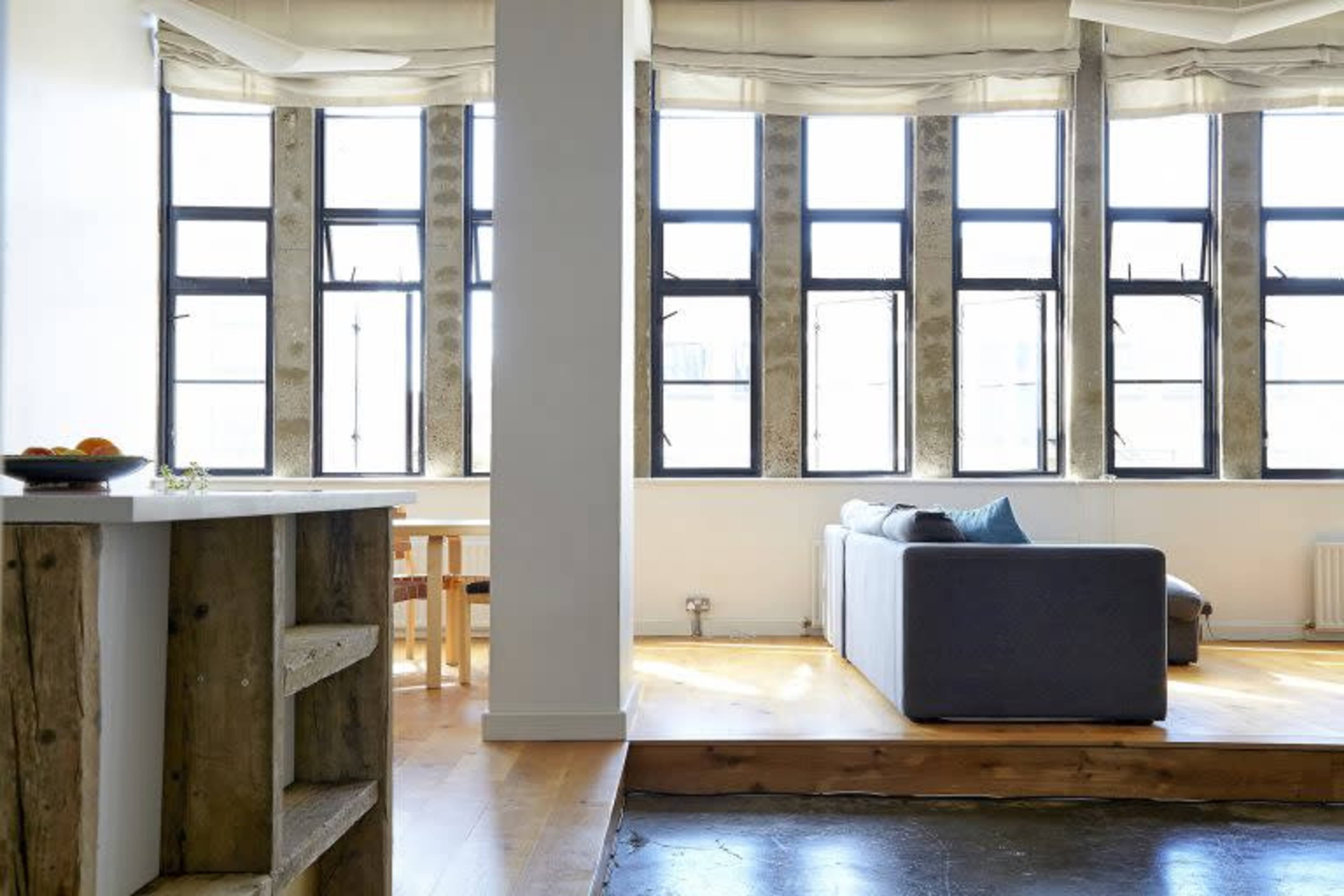The image shows a modern interior space featuring large windows with multiple panes, a sofa, and a small dining table with chairs.