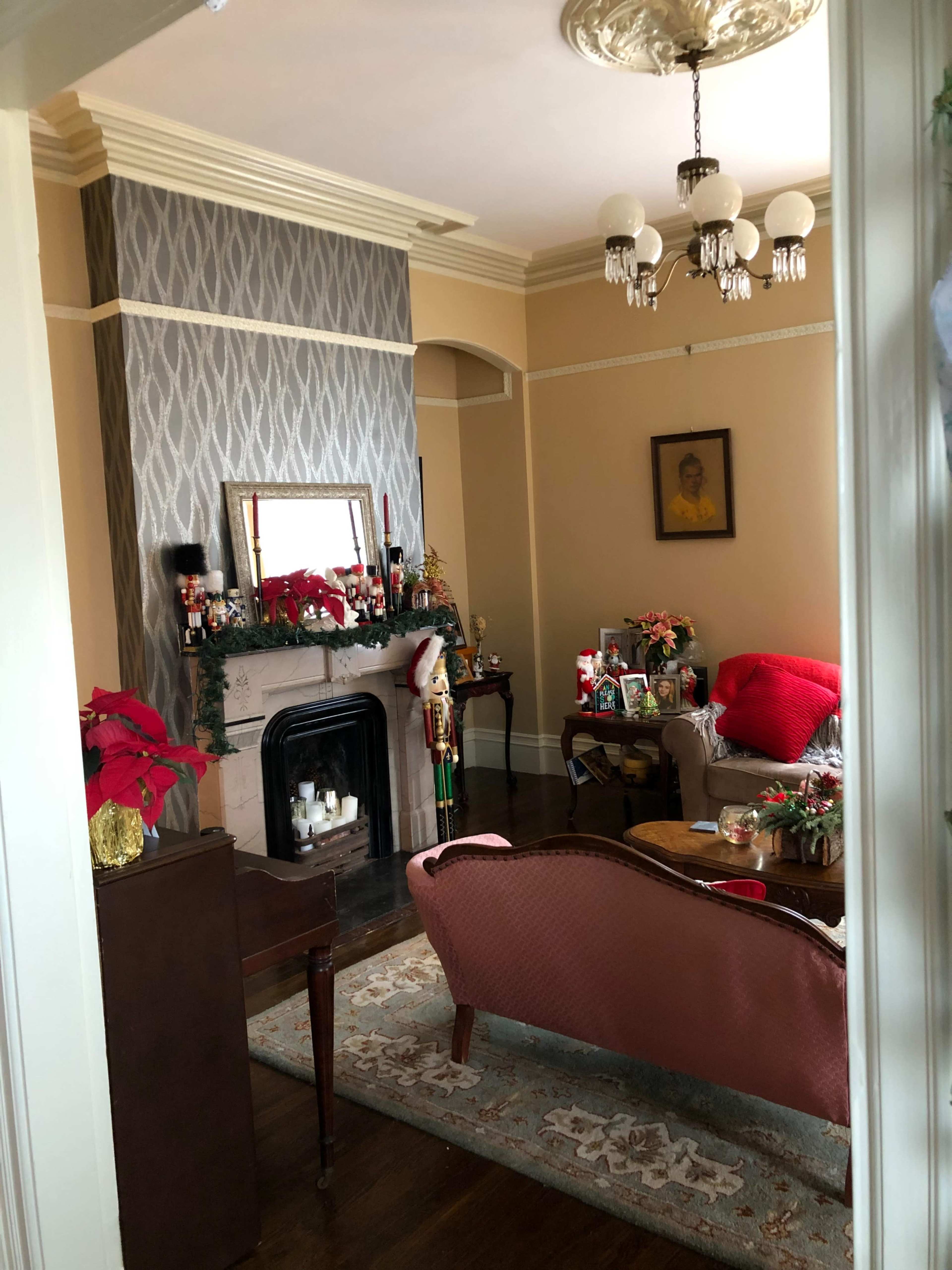A cozy living room decorated for the holidays, featuring a fireplace, a vintage-style sofa, and festive arrangements on tables and shelves.