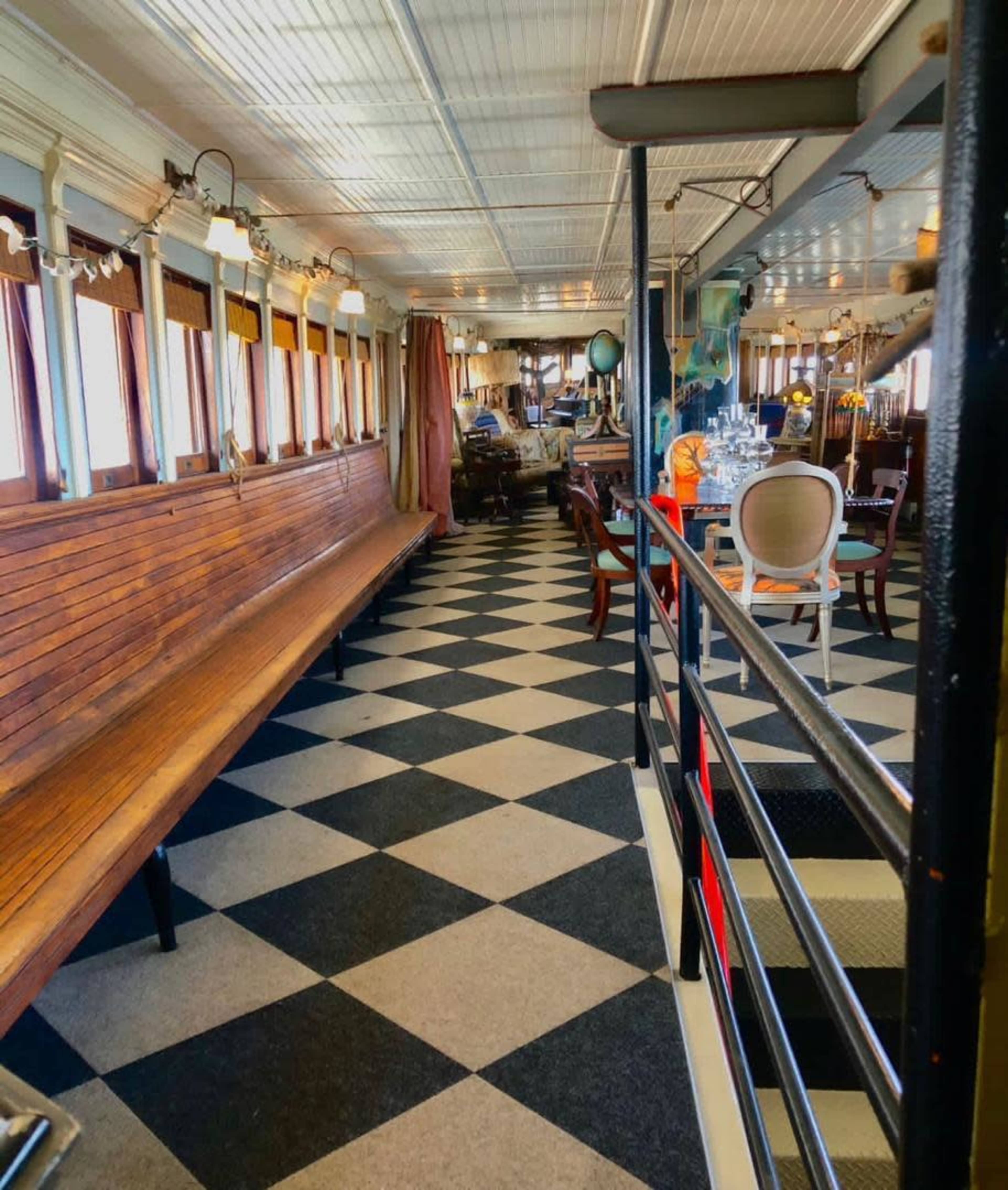 The image shows the interior of a vintage-style boat, featuring a checkerboard floor and wooden benches along the walls.