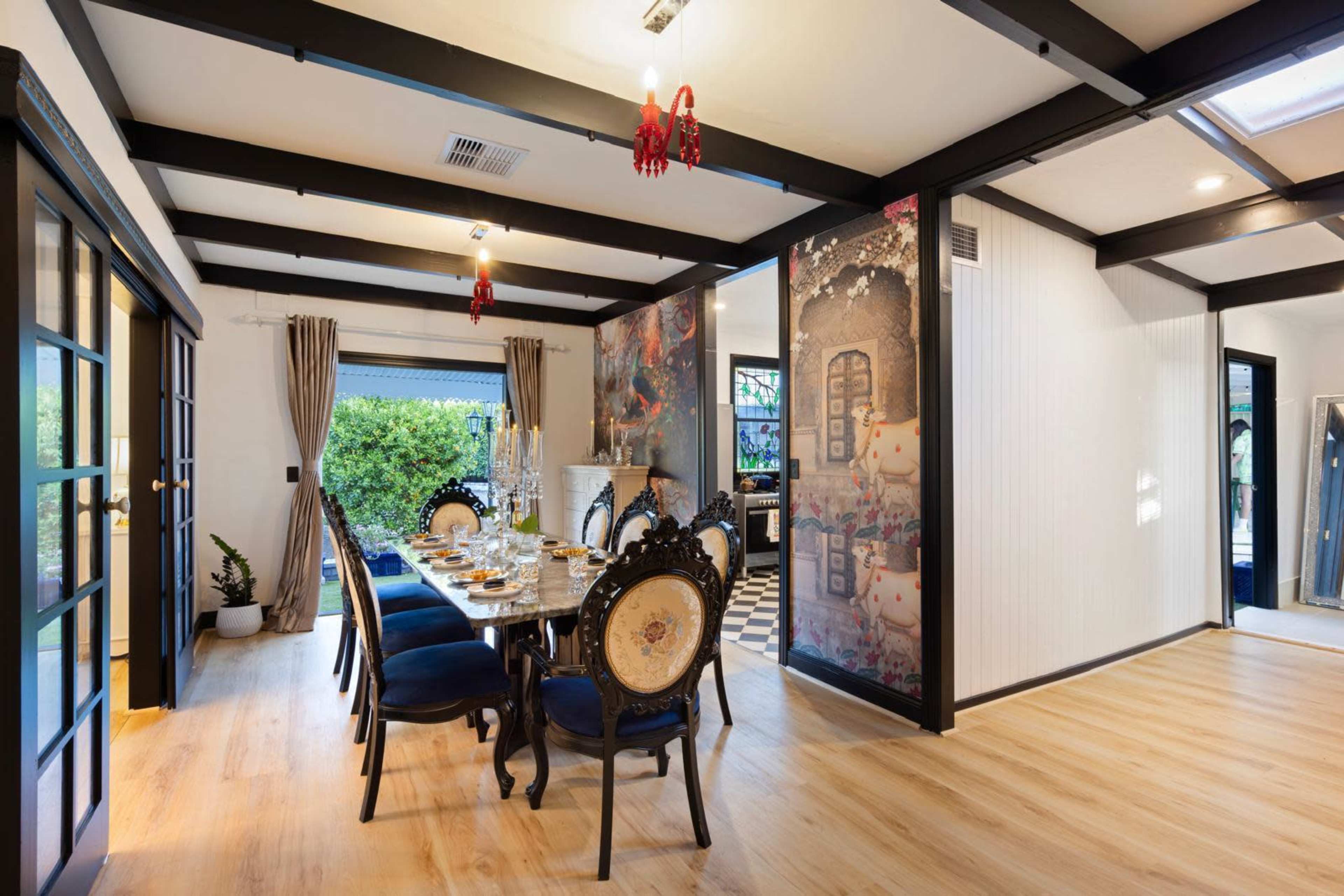 The image depicts a dining room with a long table set for a meal, surrounded by elegant chairs, and adorned with decorative wall art and large windows.
