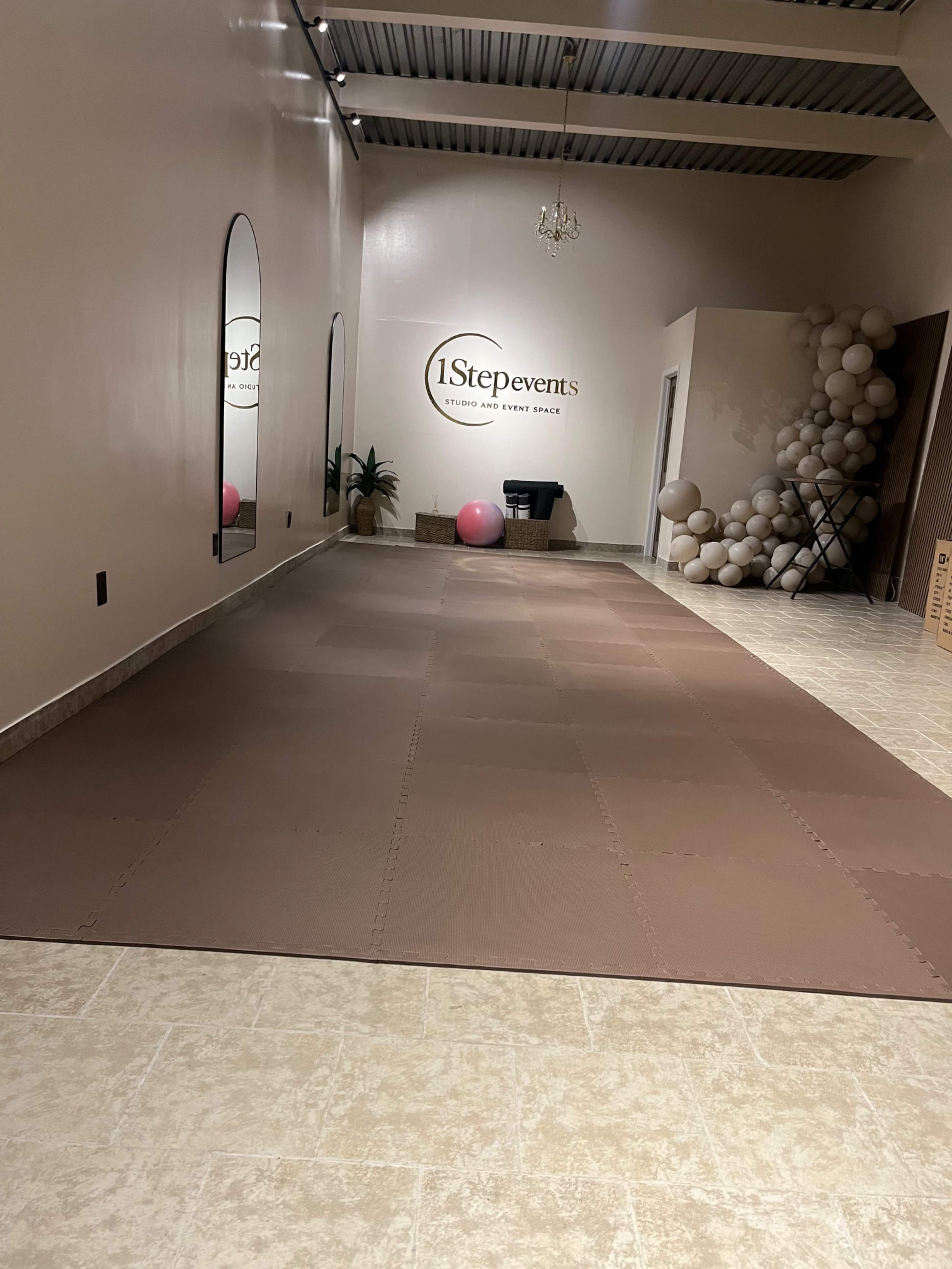 The image shows a spacious event studio with a brown padded floor, mirrors on one wall, and a large sign reading "1StepEvents" along with a decorative balloon arrangement in the corner.