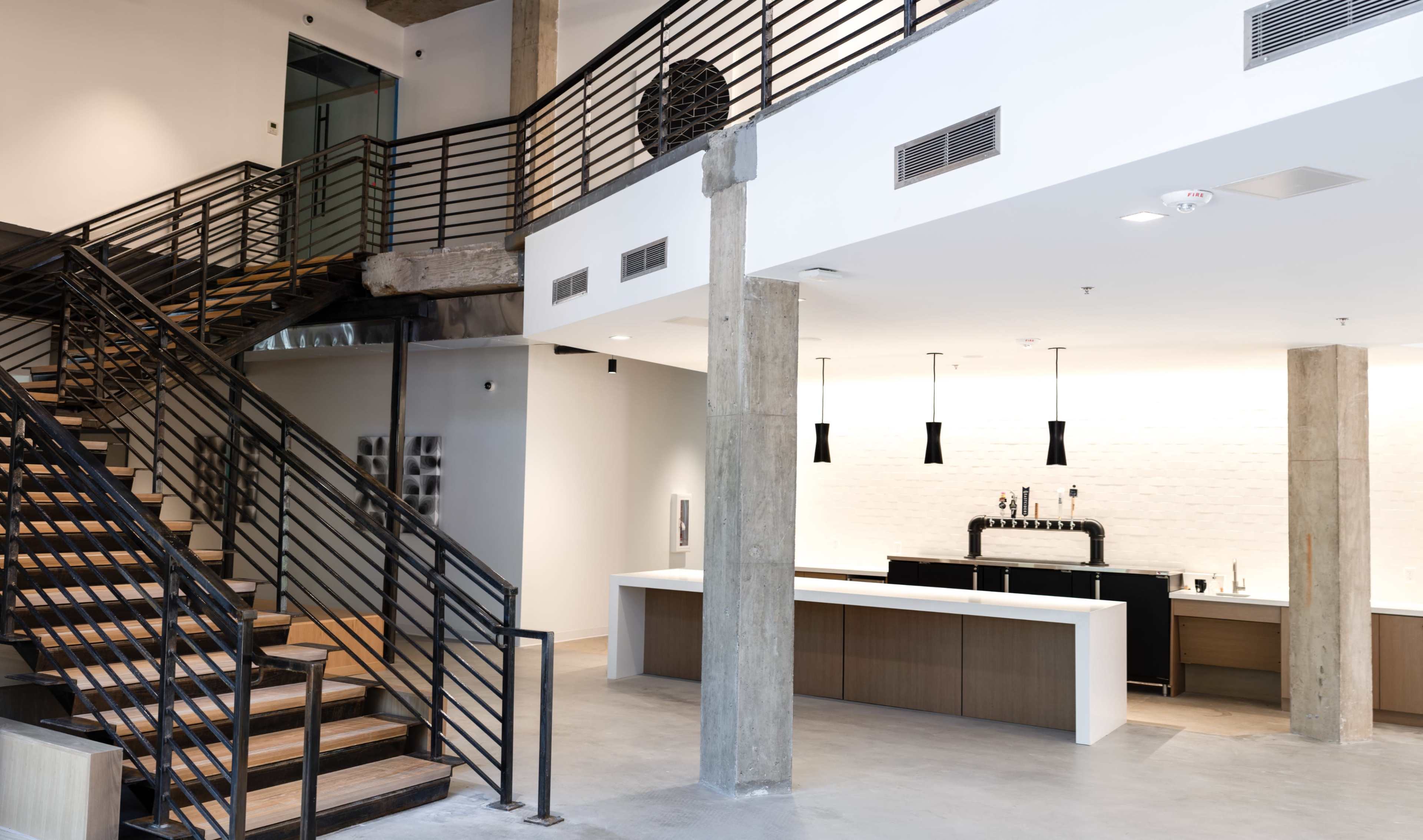 A spacious interior with a modern staircase, featuring metal railings, leading to a second level adjacent to a sleek bar area with minimalistic design elements.