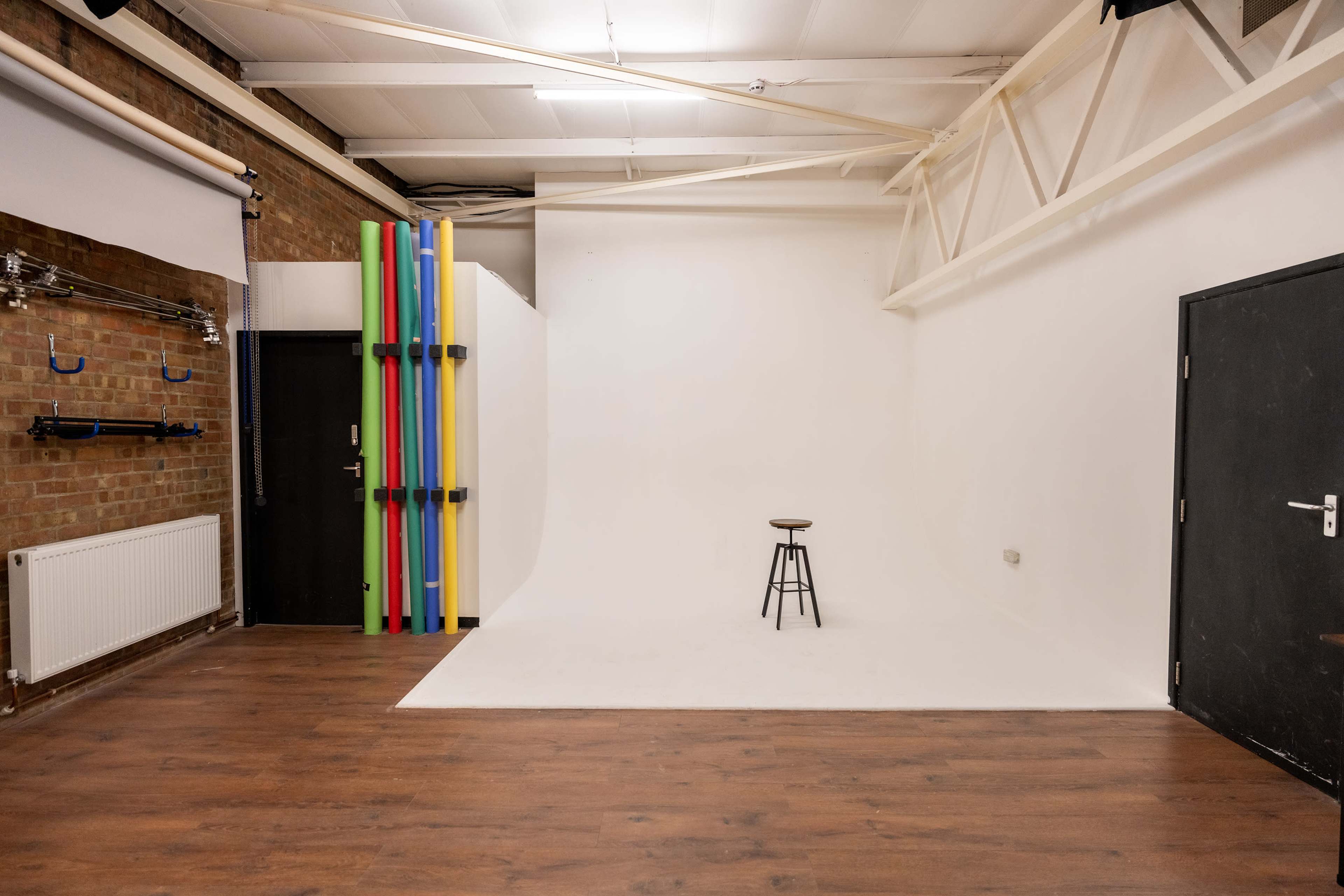 A spacious photography studio with a white backdrop, a wooden floor, and a single stool in the center.