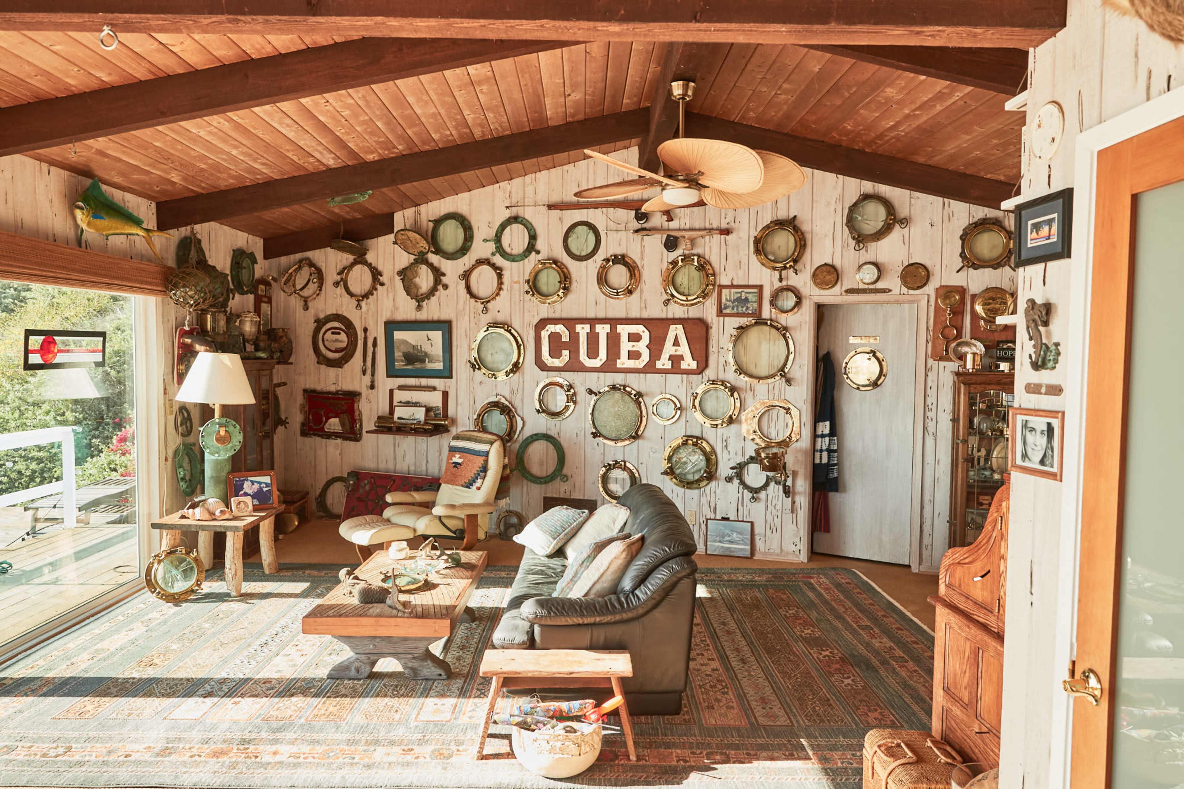 A cozy living room features a variety of round mirrors and decorations mounted on the wooden walls, with a prominent "CUBA" sign in the center.