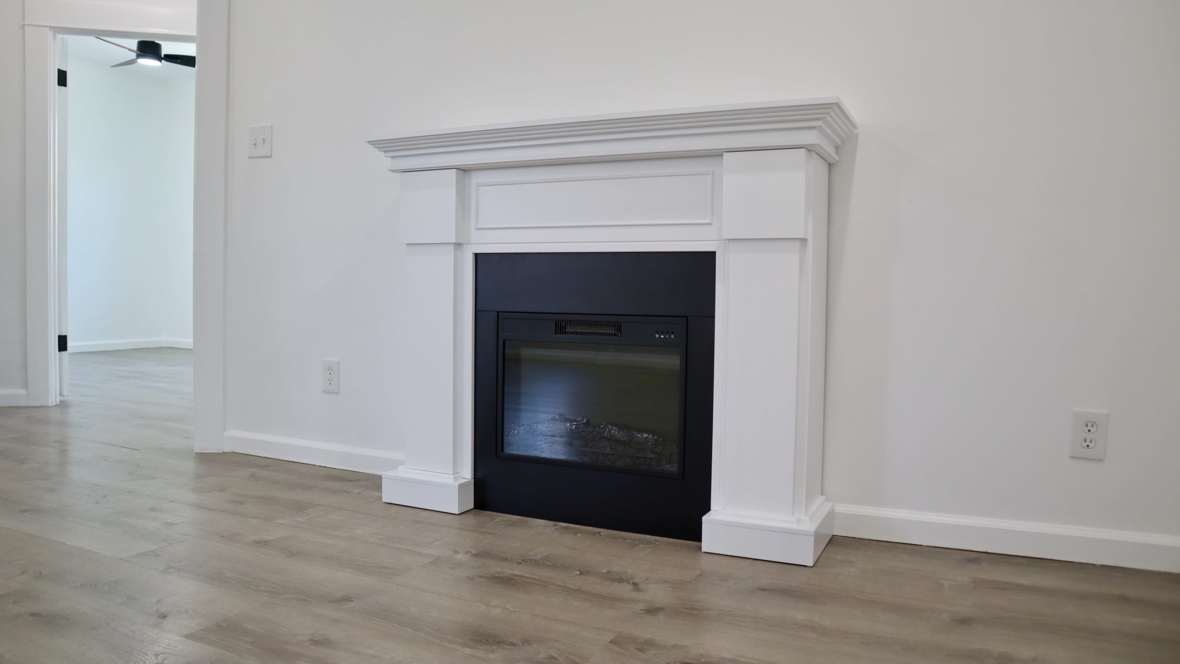 A modern, white mantel surrounding a black electric fireplace against a plain white wall.