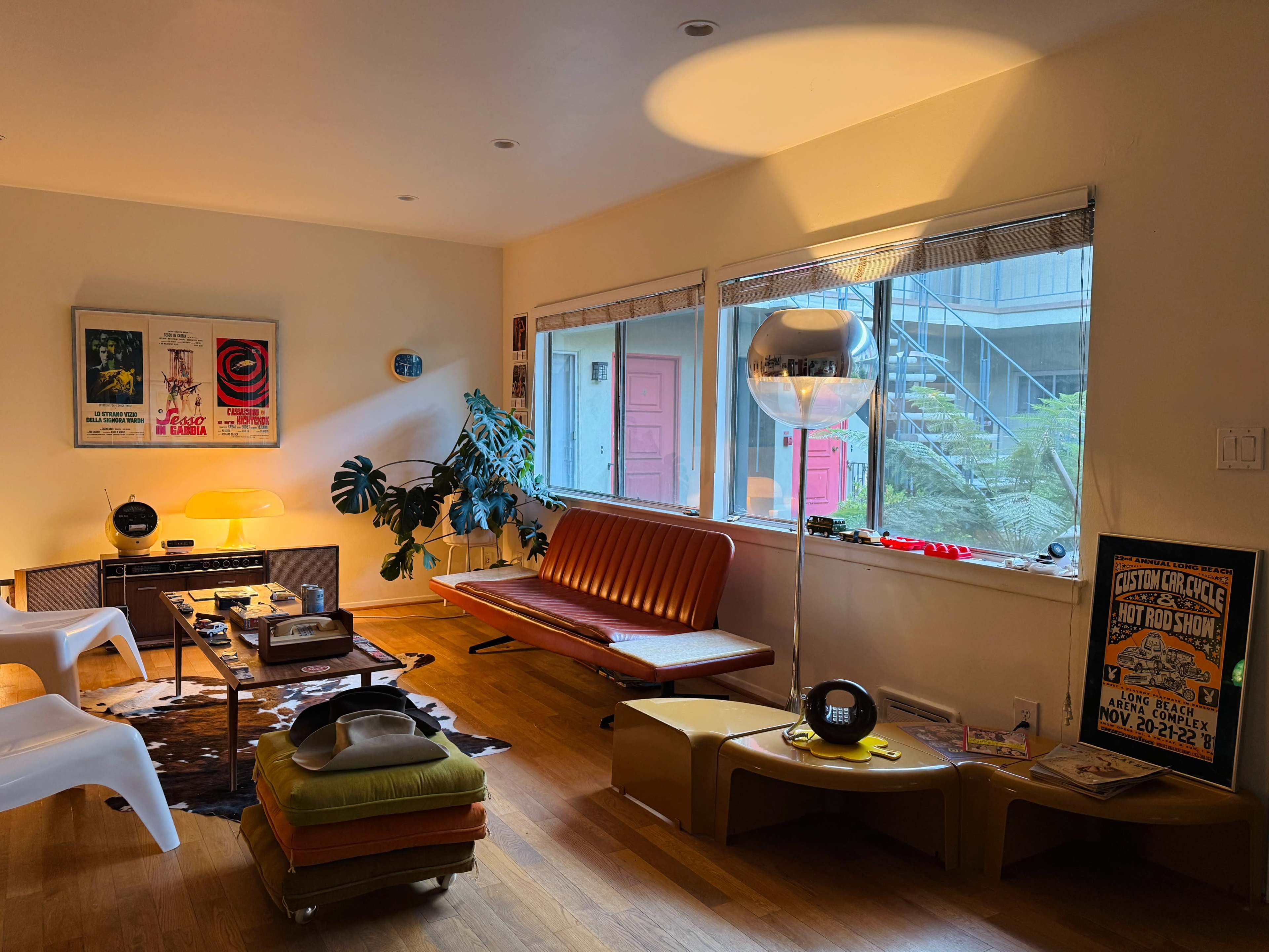 A mid-century modern living room features a retro orange couch, a round mirror lamp, and large windows illuminating the space with natural light.