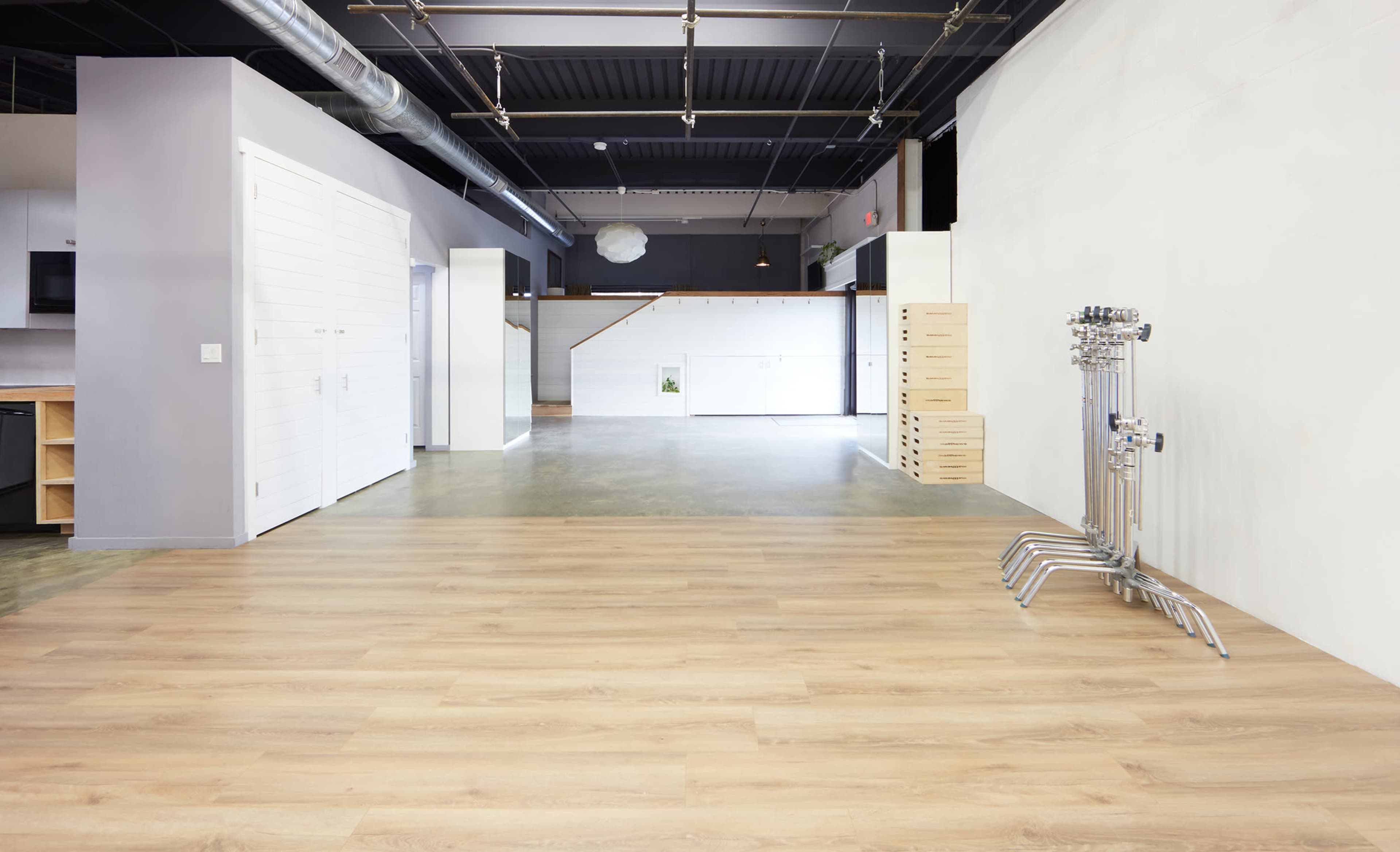 A spacious, modern interior with polished wood flooring, white walls, and a minimalist design featuring open areas and a staircase in the background.