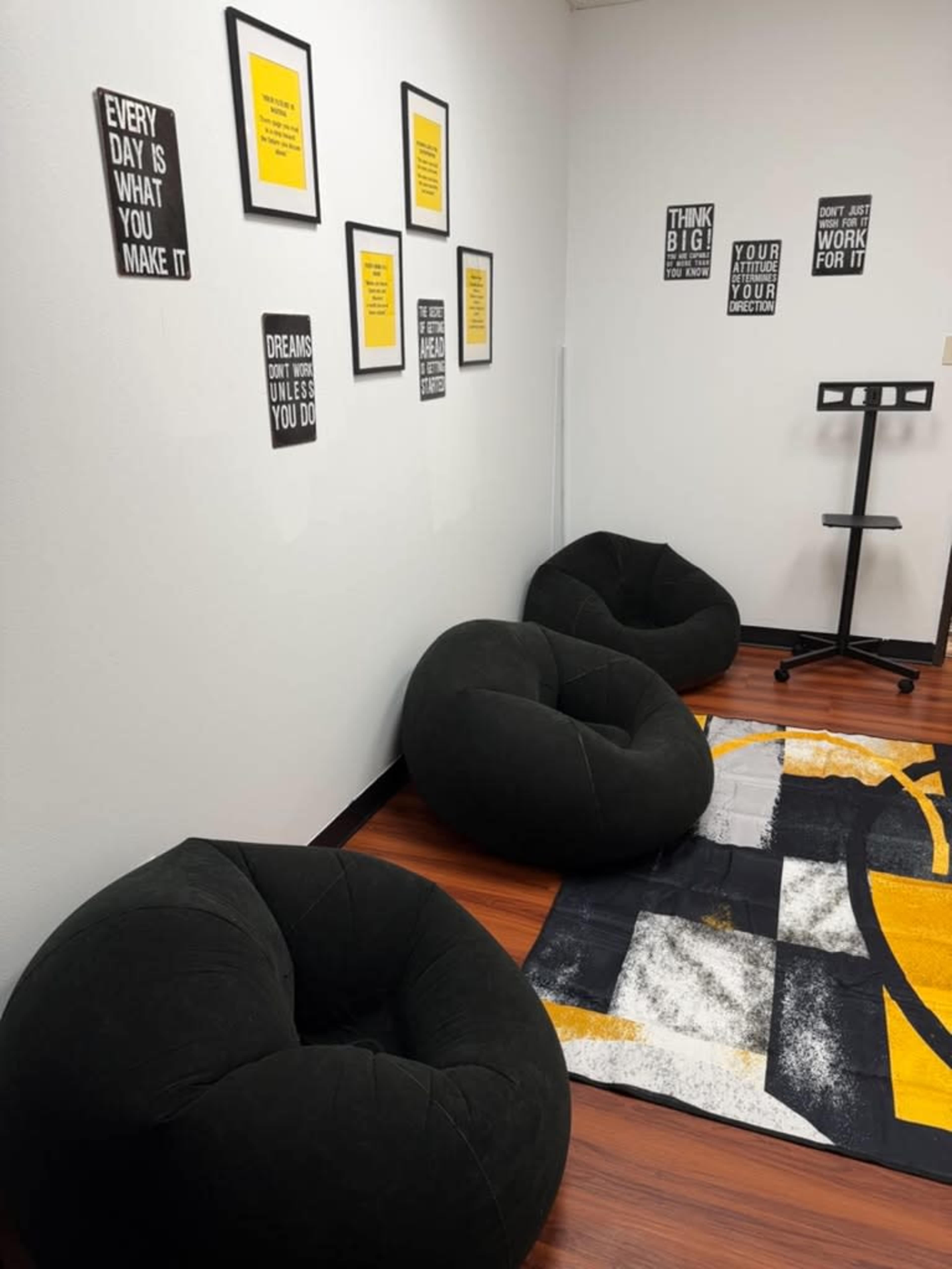 The image shows a corner of a room with three black bean bag chairs, a patterned rug, and several motivational quotes framed on the walls.