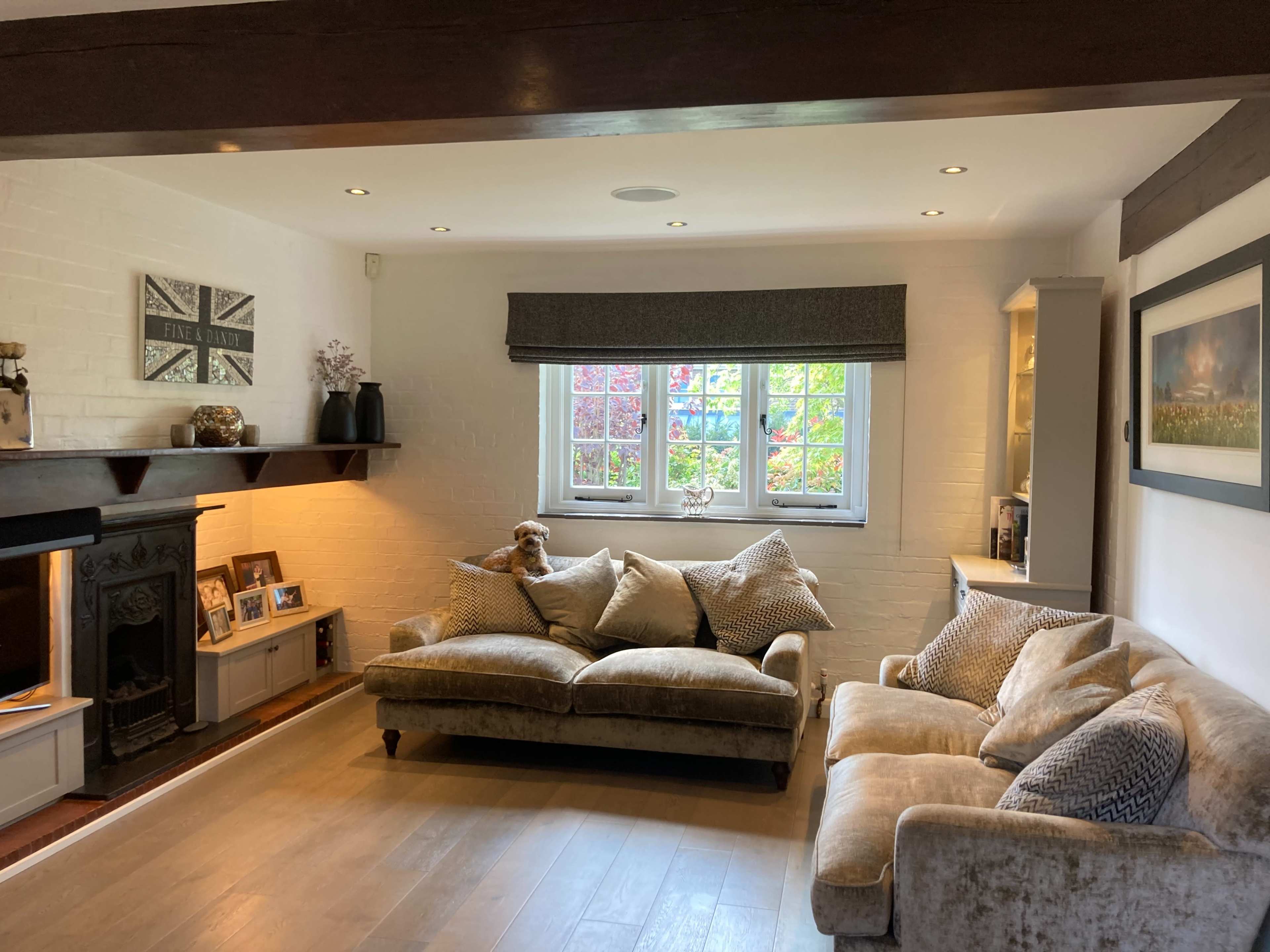 A living room with a comfortable beige sofa, a plush armchair, and a decorative wall with a fireplace and various framed pictures.