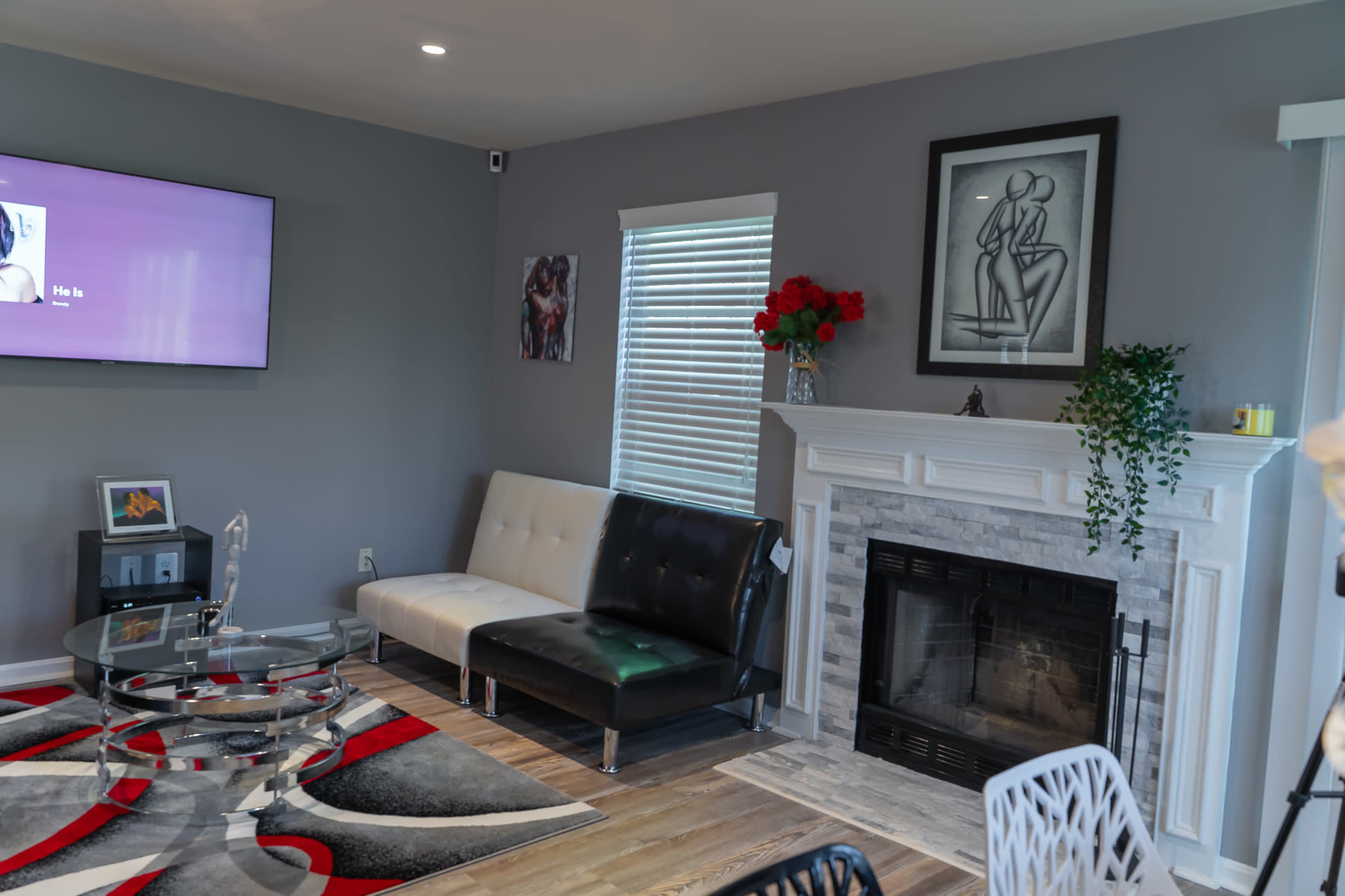 A modern living room featuring a two-tone sofa, a glass coffee table, a fireplace, and decorative art on the walls.