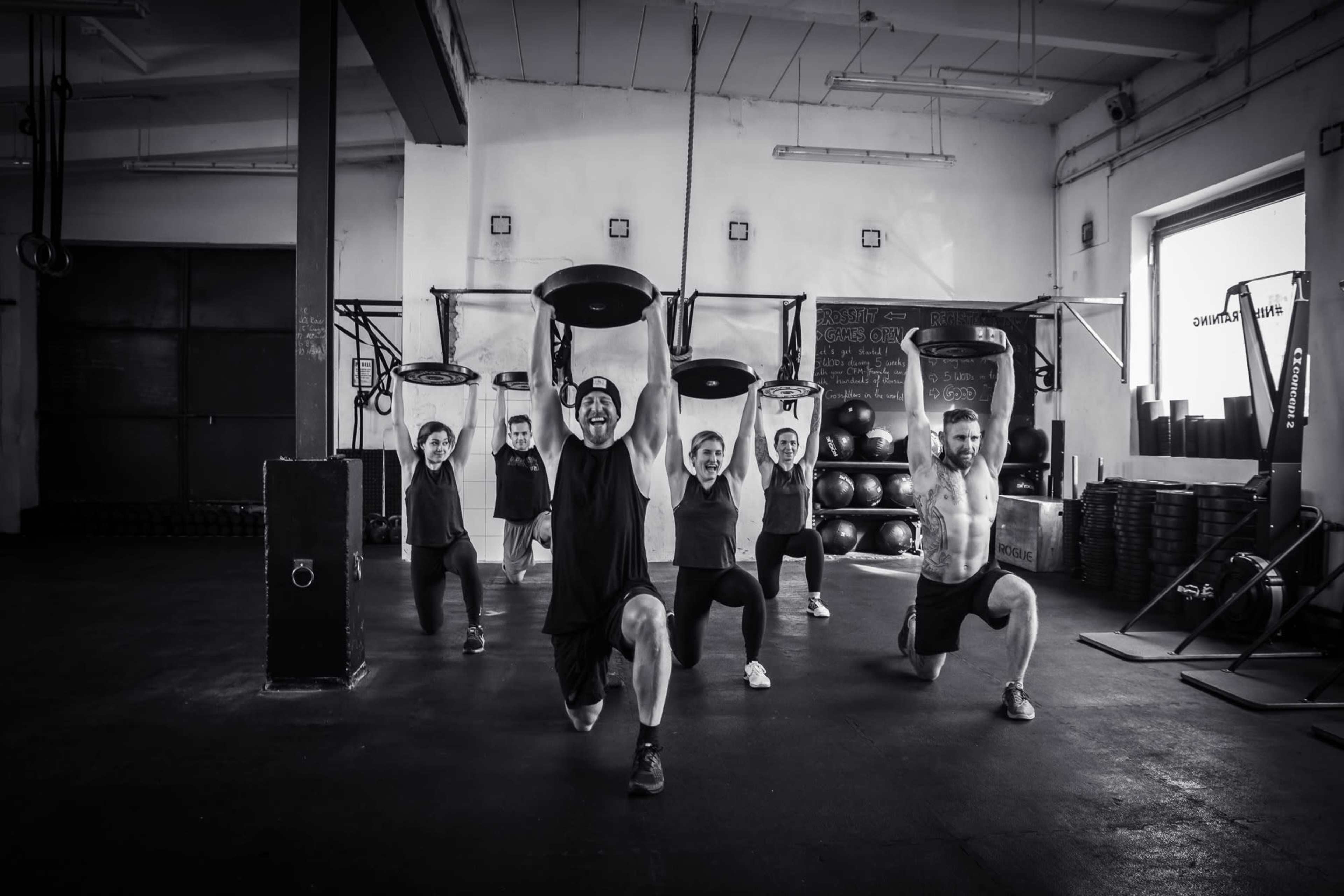 A group of six individuals performs lunges while holding weighted plates in a gym setting.