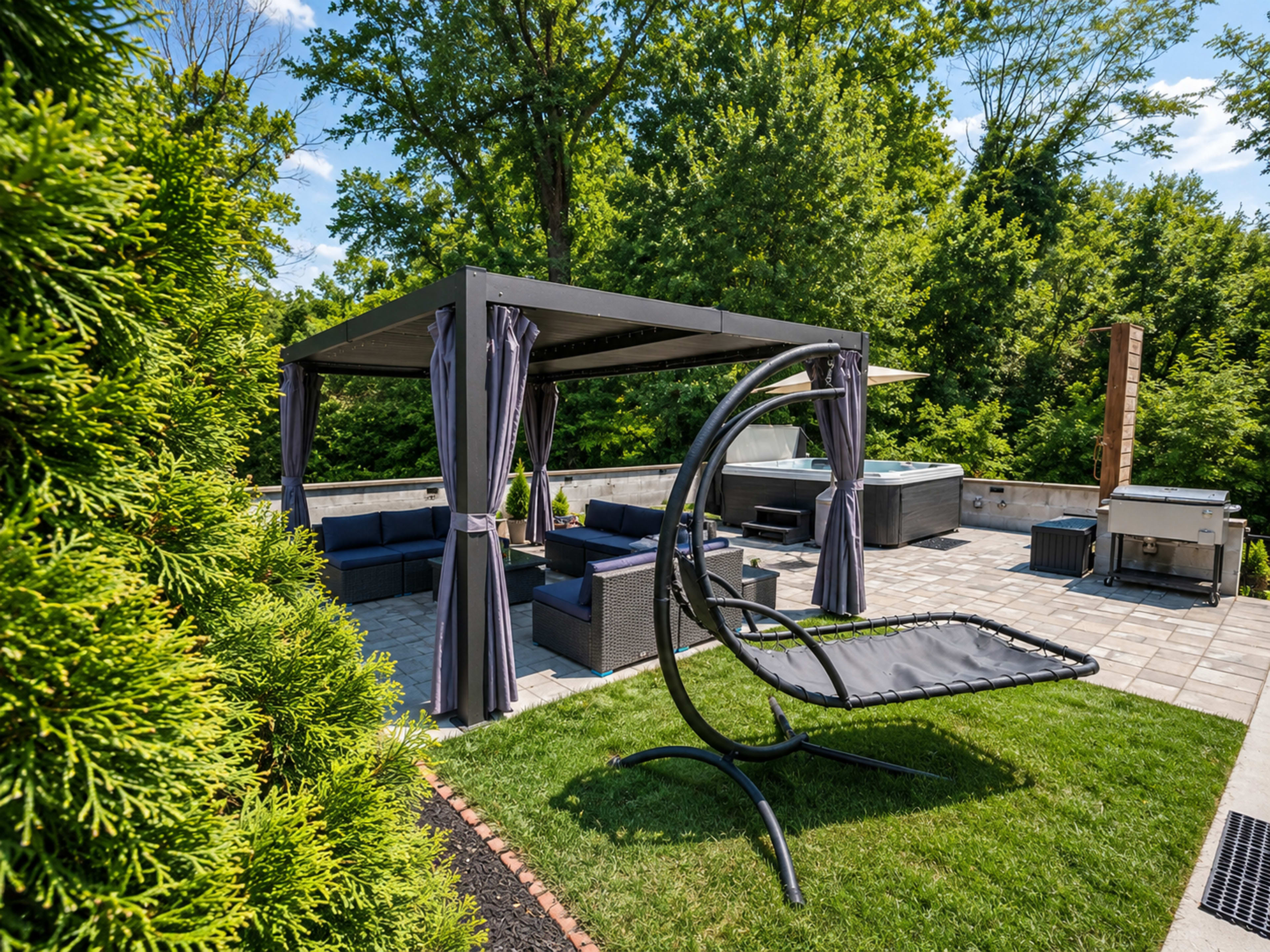 The image shows a patio area with a shaded seating arrangement, a hanging lounge chair, and hot tubs surrounded by greenery.