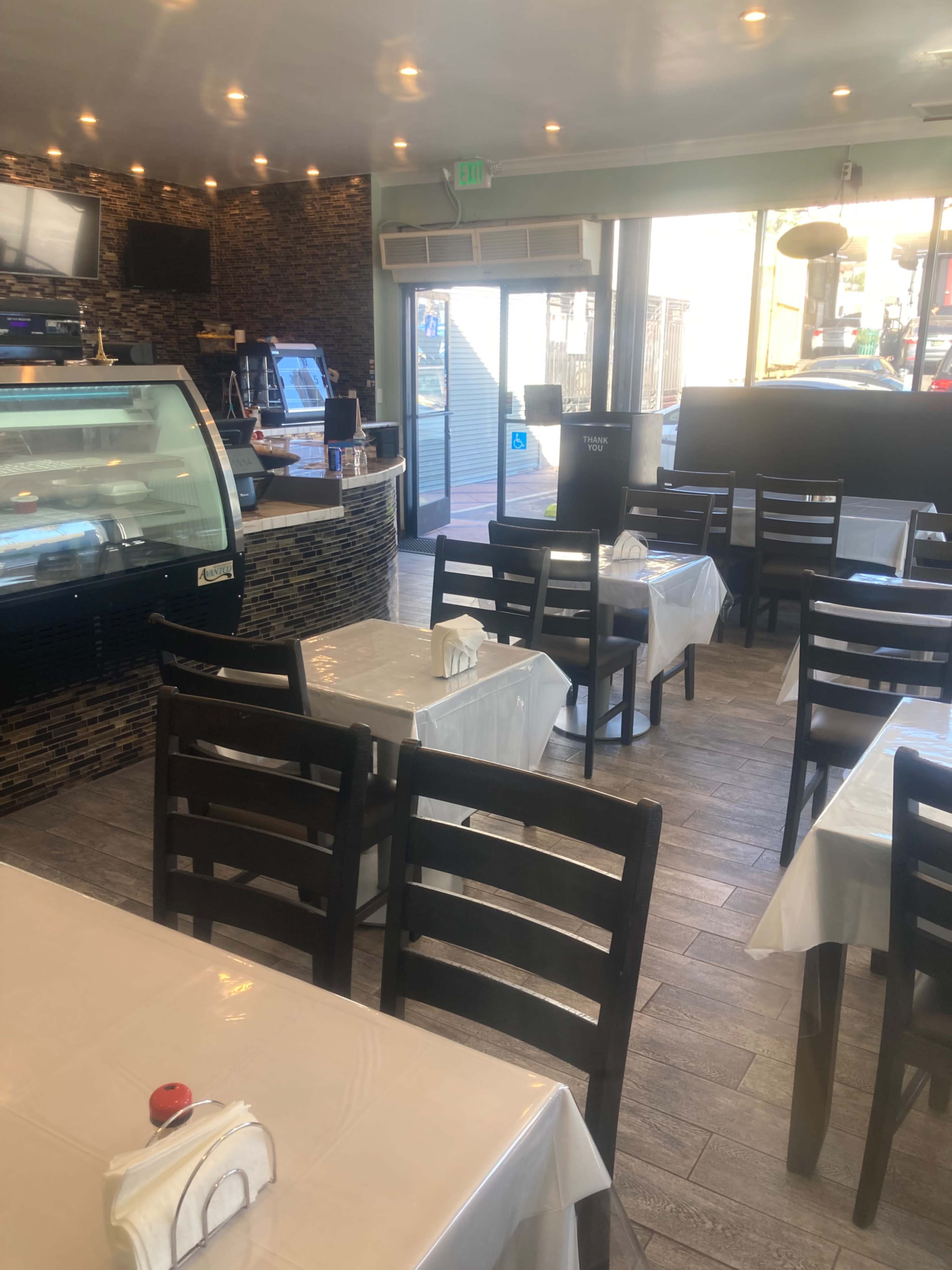 The image shows a dining area of a restaurant with multiple tables covered in white tablecloths and a display case in the background.