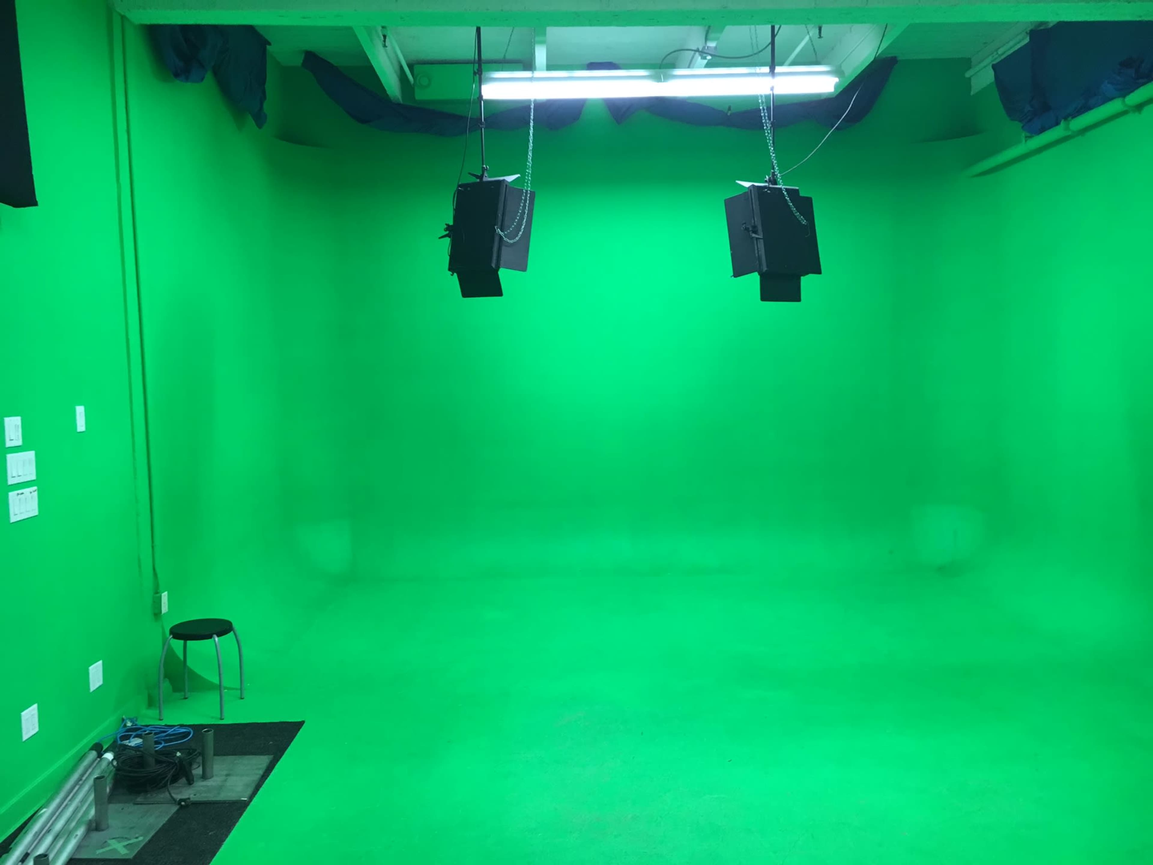 A green screen studio with two overhead lights and a solitary stool.
