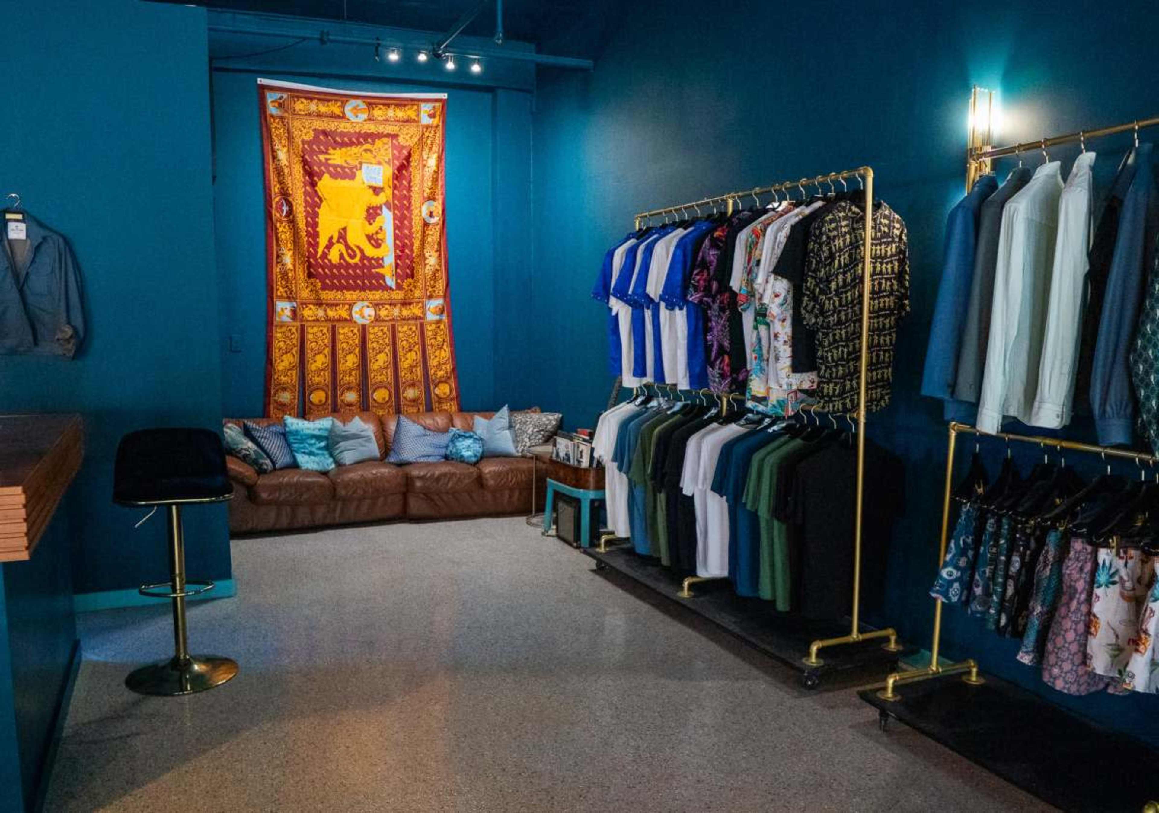 The image shows a retail clothing store with a sofa and decorative wall hanging, along with clothing racks displaying a variety of shirts.