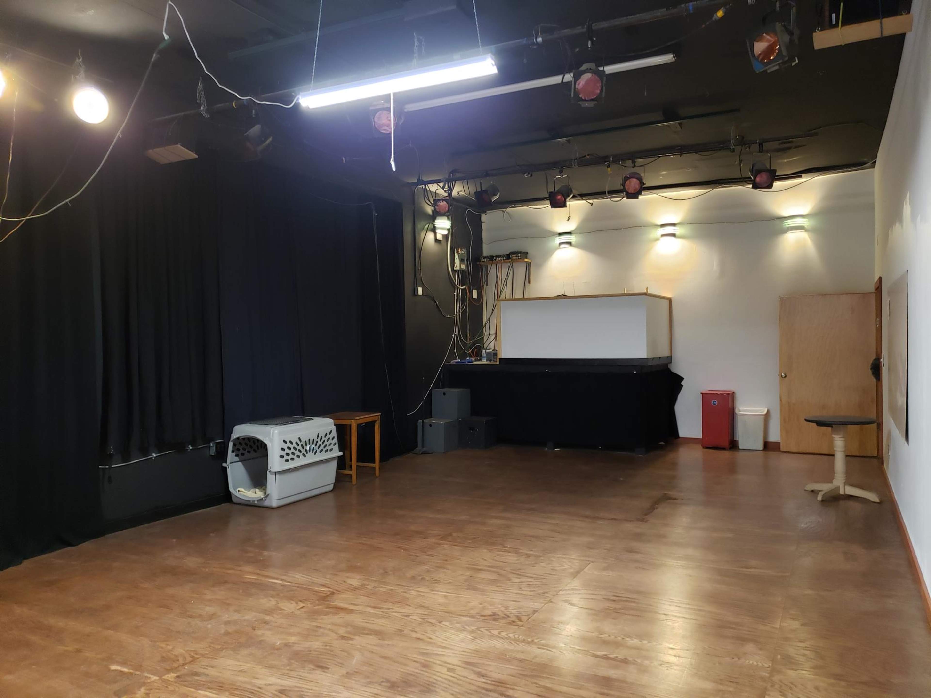 An empty performance space with black curtains, wooden floors, and various lighting fixtures.
