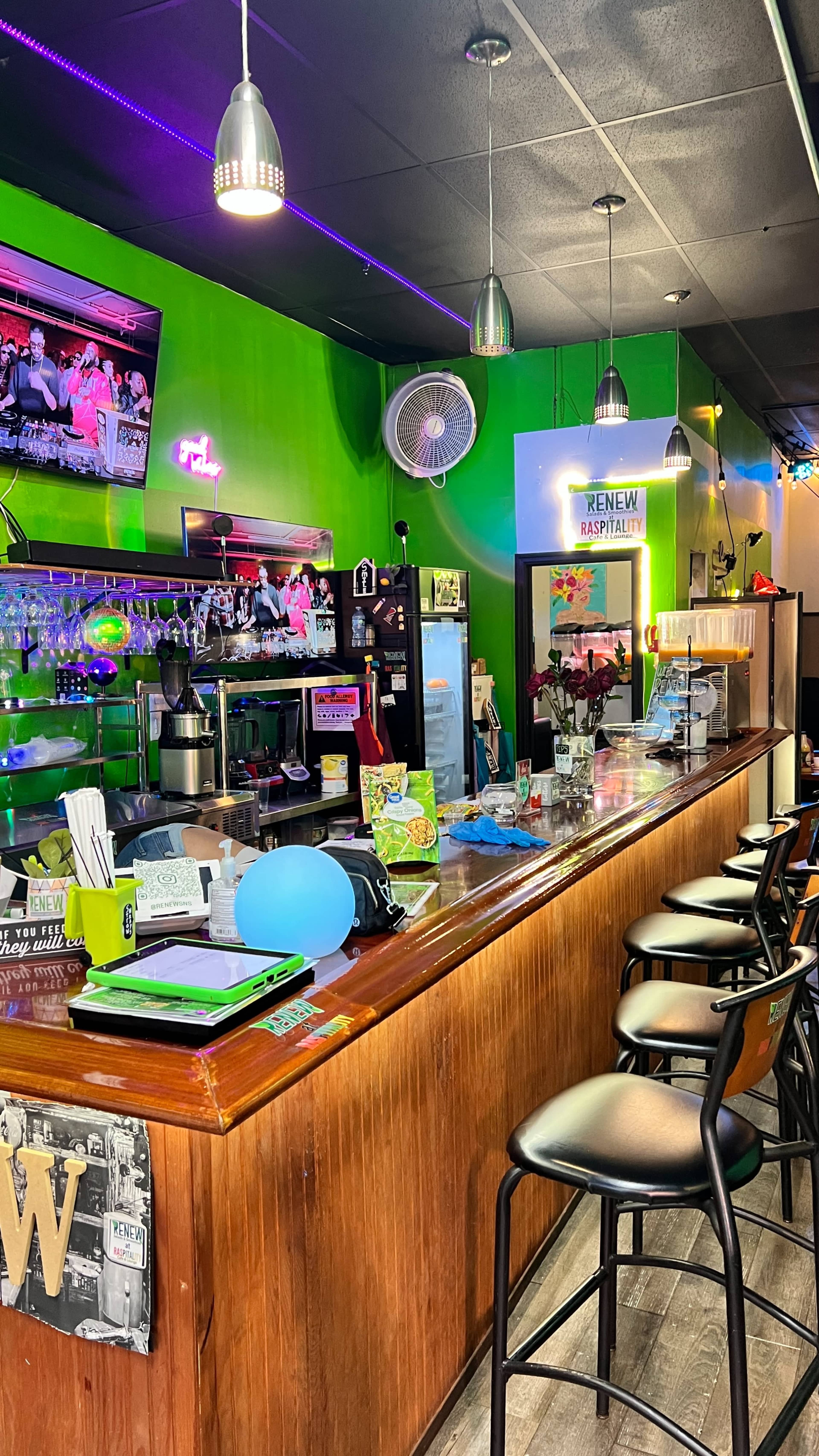 The image shows a brightly colored bar area with a counter, stools, and various items displayed, including a television and a fan.