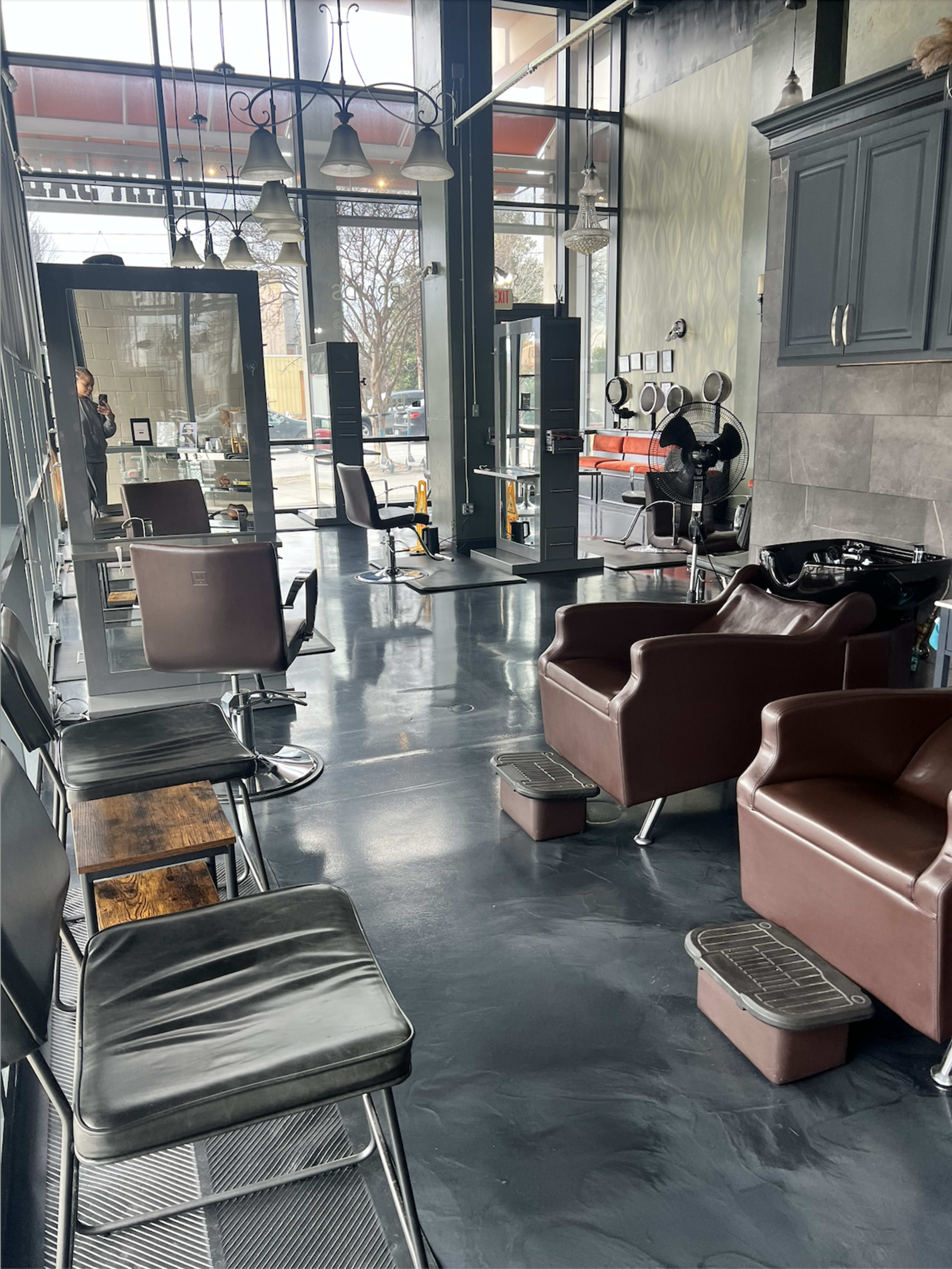 The image shows a modern hair salon with several styling chairs, shampoo stations, and large windows allowing natural light to fill the space.