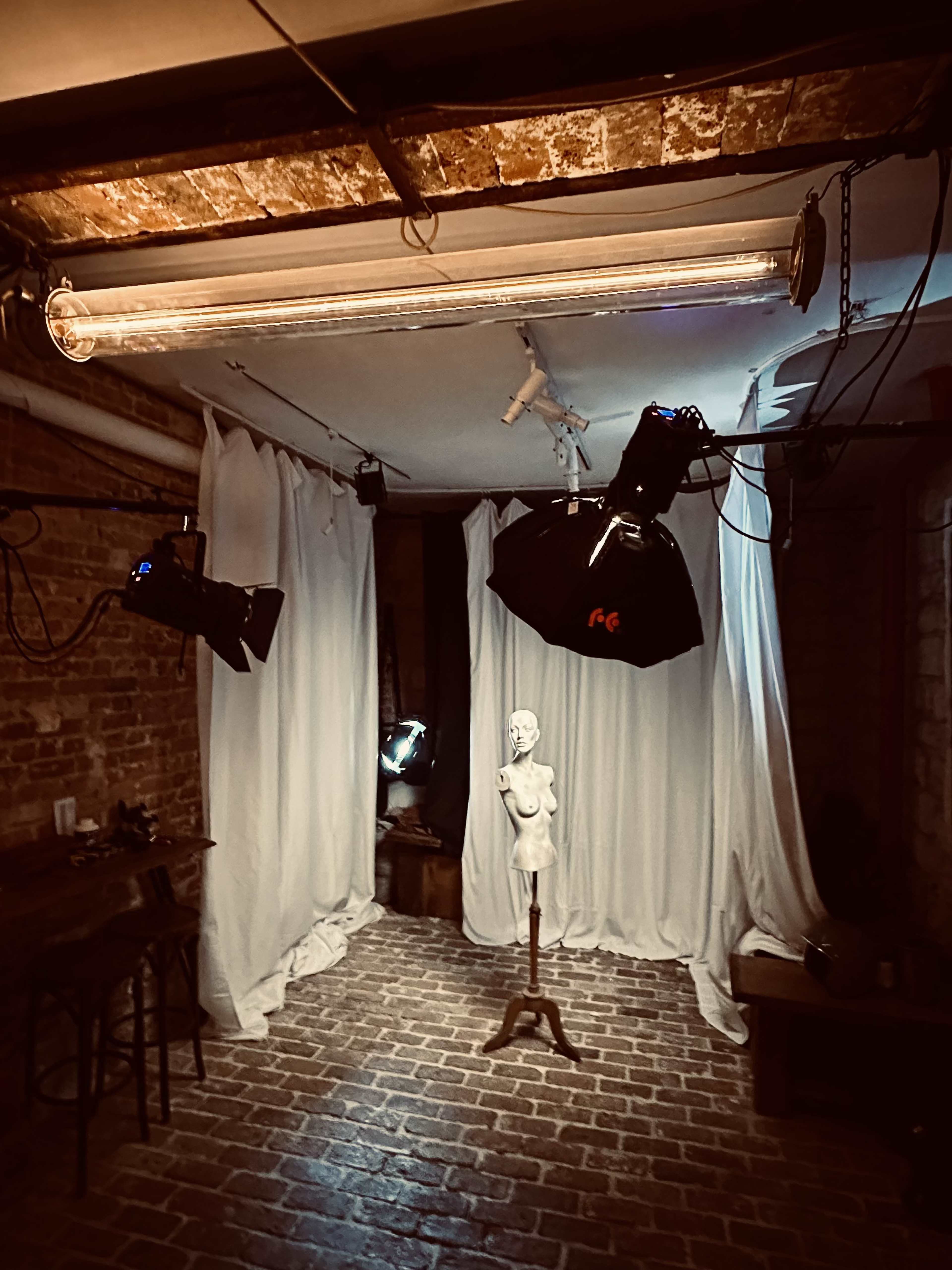 A photography studio with a classical bust on a pedestal surrounded by draped white fabric and lighting equipment.