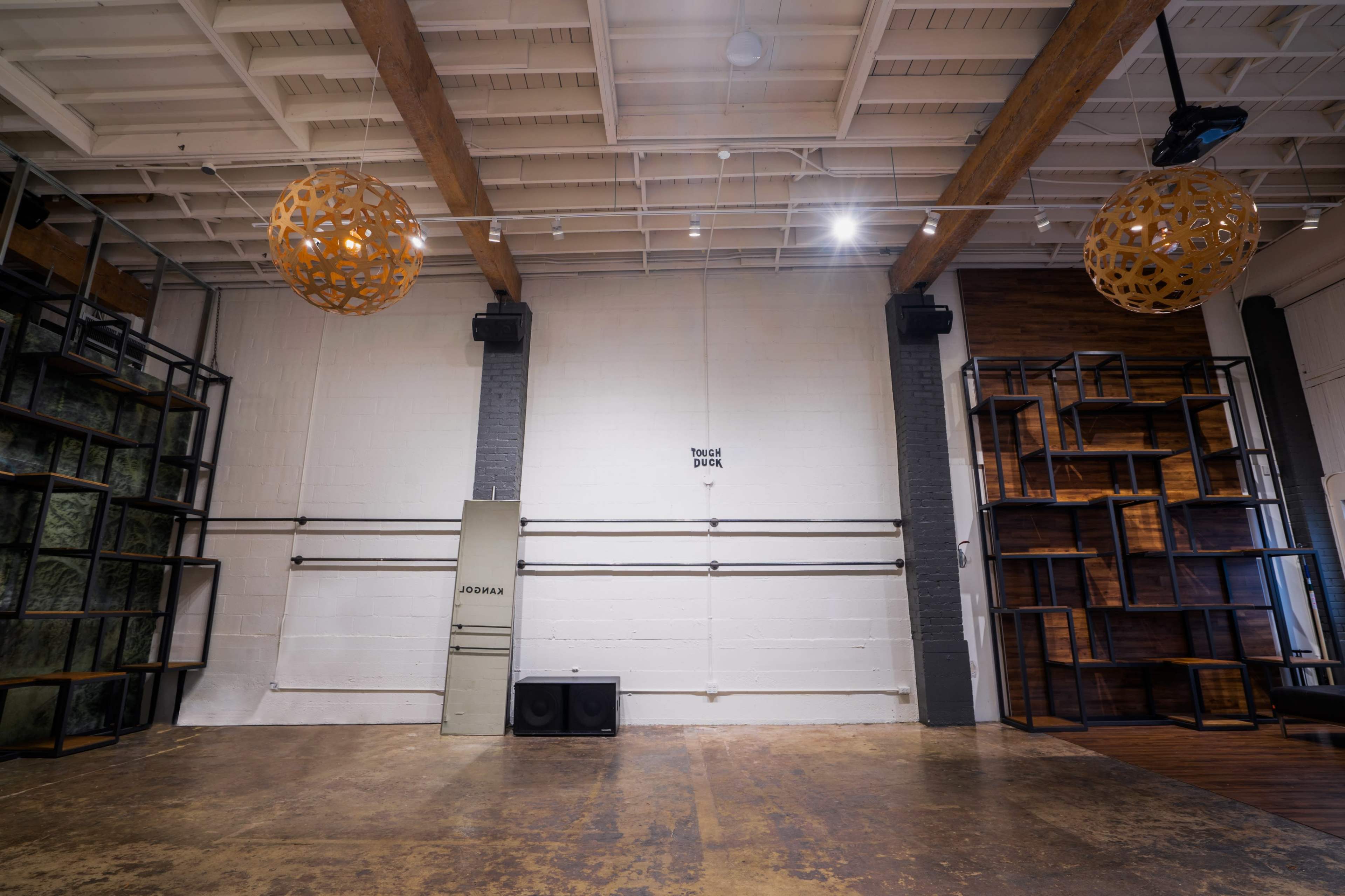 The interior space features wooden beams, modern light fixtures, and a combination of shelving units against the walls.