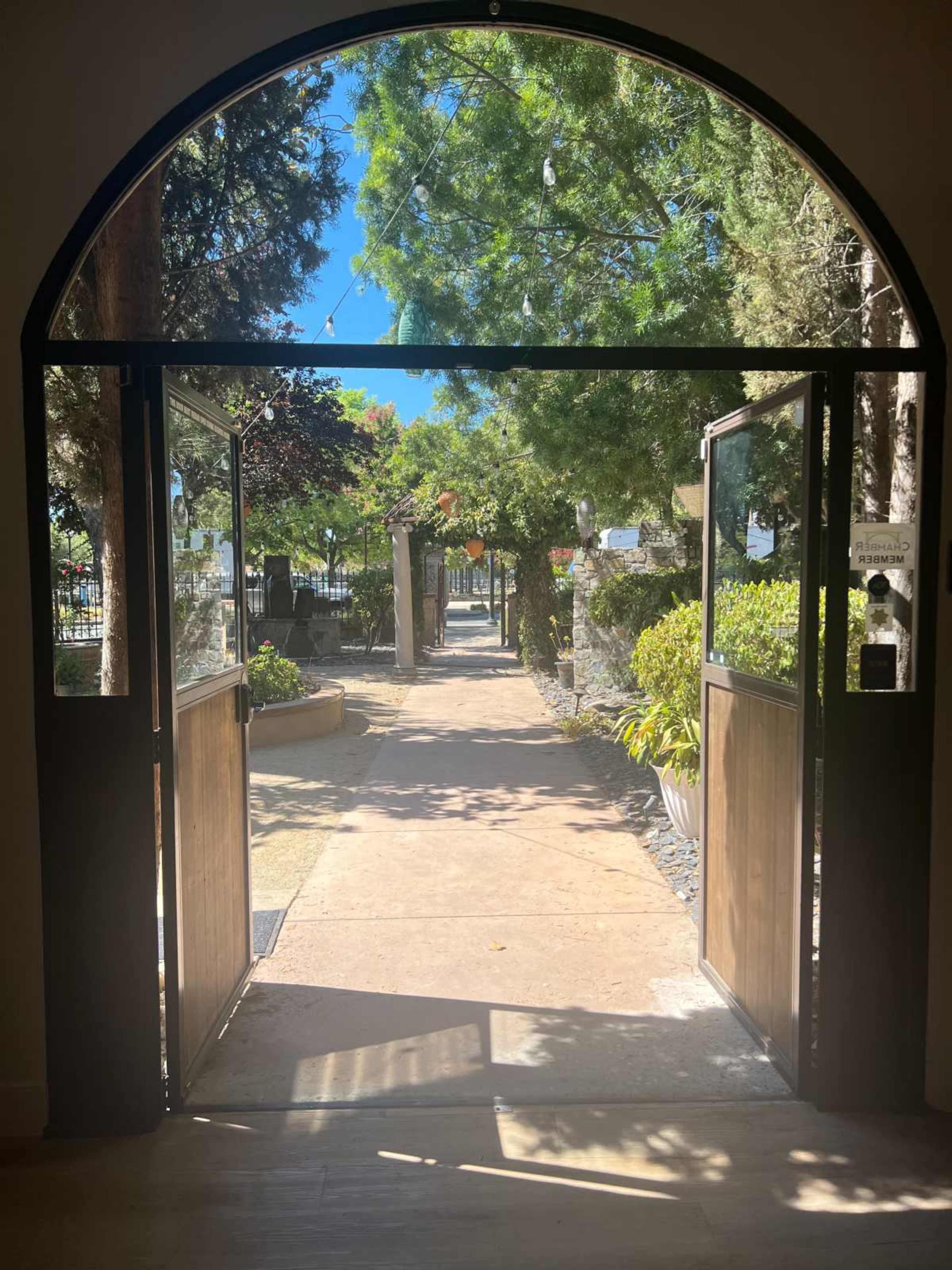 An open entrance gate leading to a pathway lined with greenery and trees.