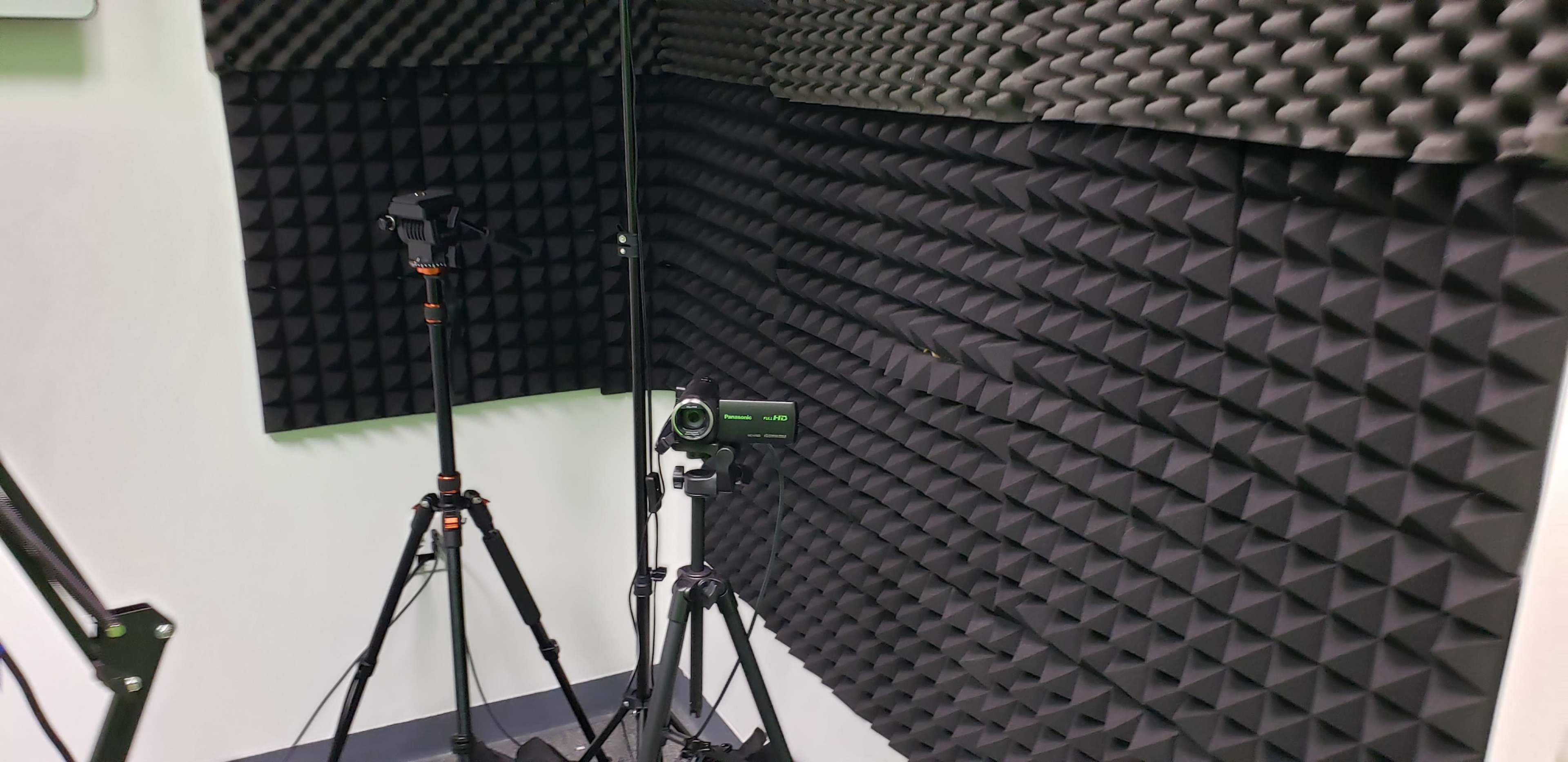 A soundproof room with two tripods holding video recording equipment against textured acoustic foam walls.