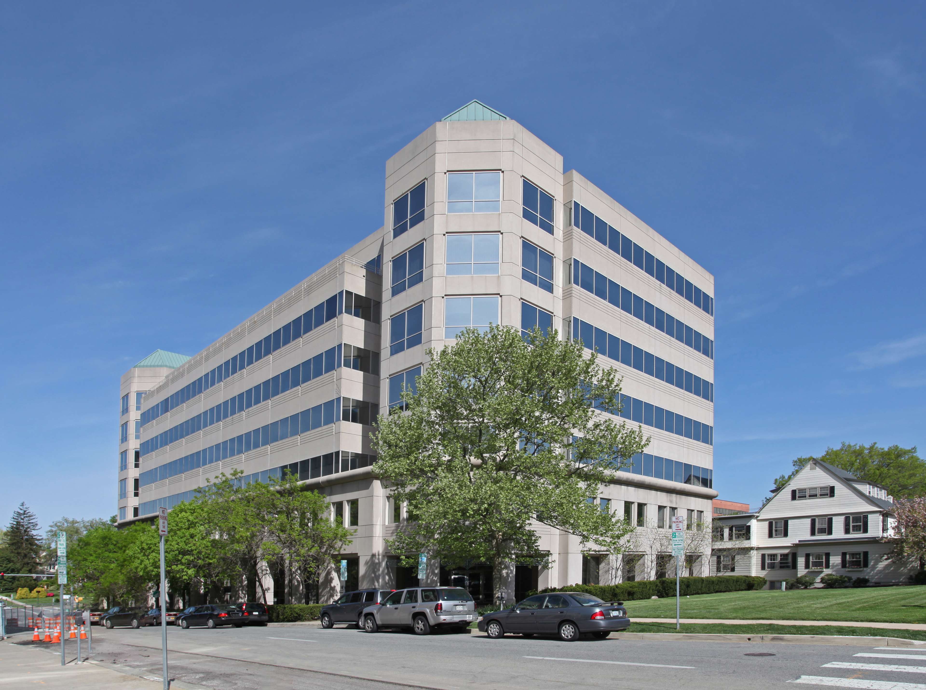 A modern six-story office building with a glass facade stands next to a residential area.