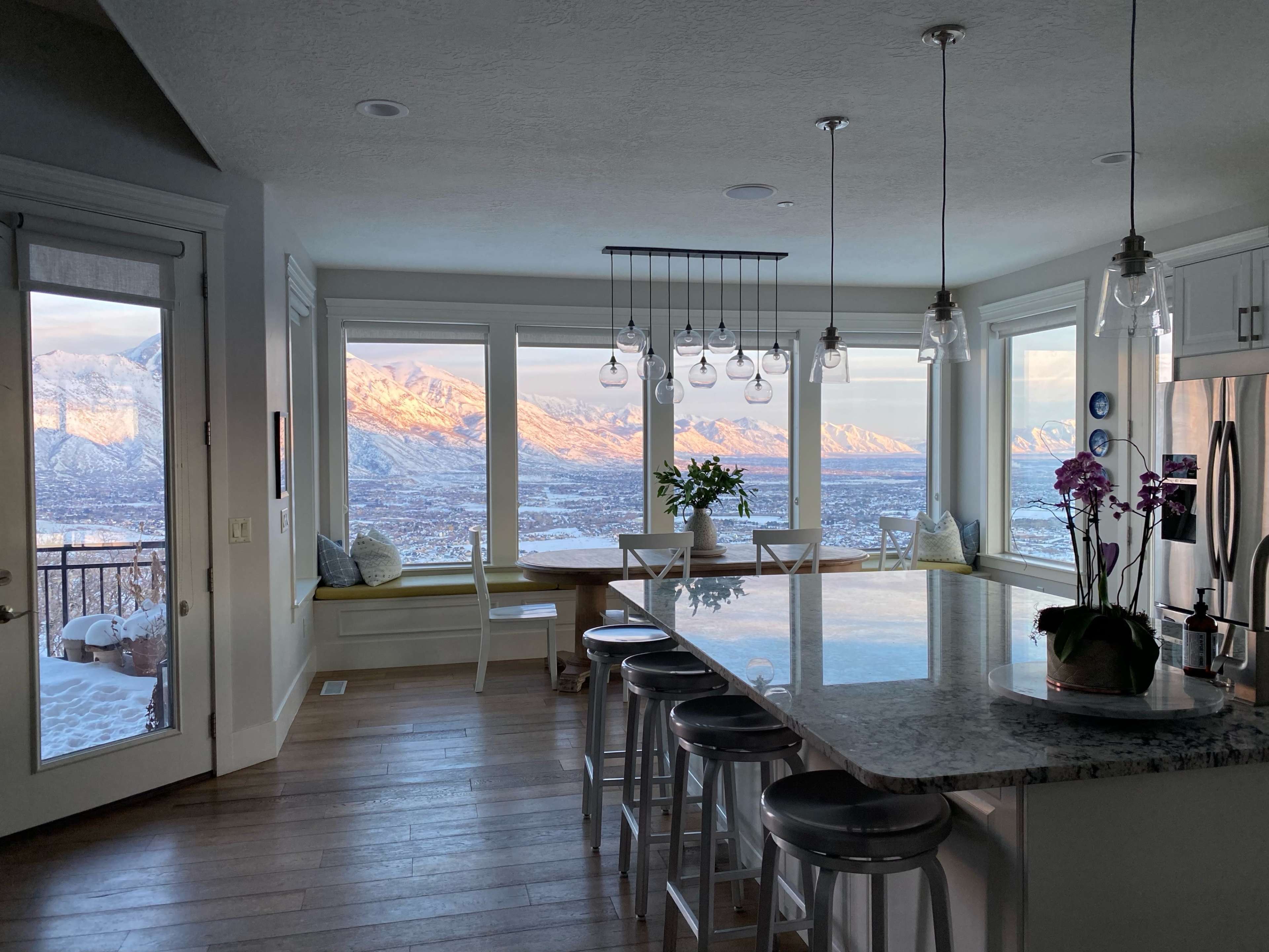 A kitchen features a large island with bar stools, surrounded by windows showcasing a mountain view with snow-capped peaks.