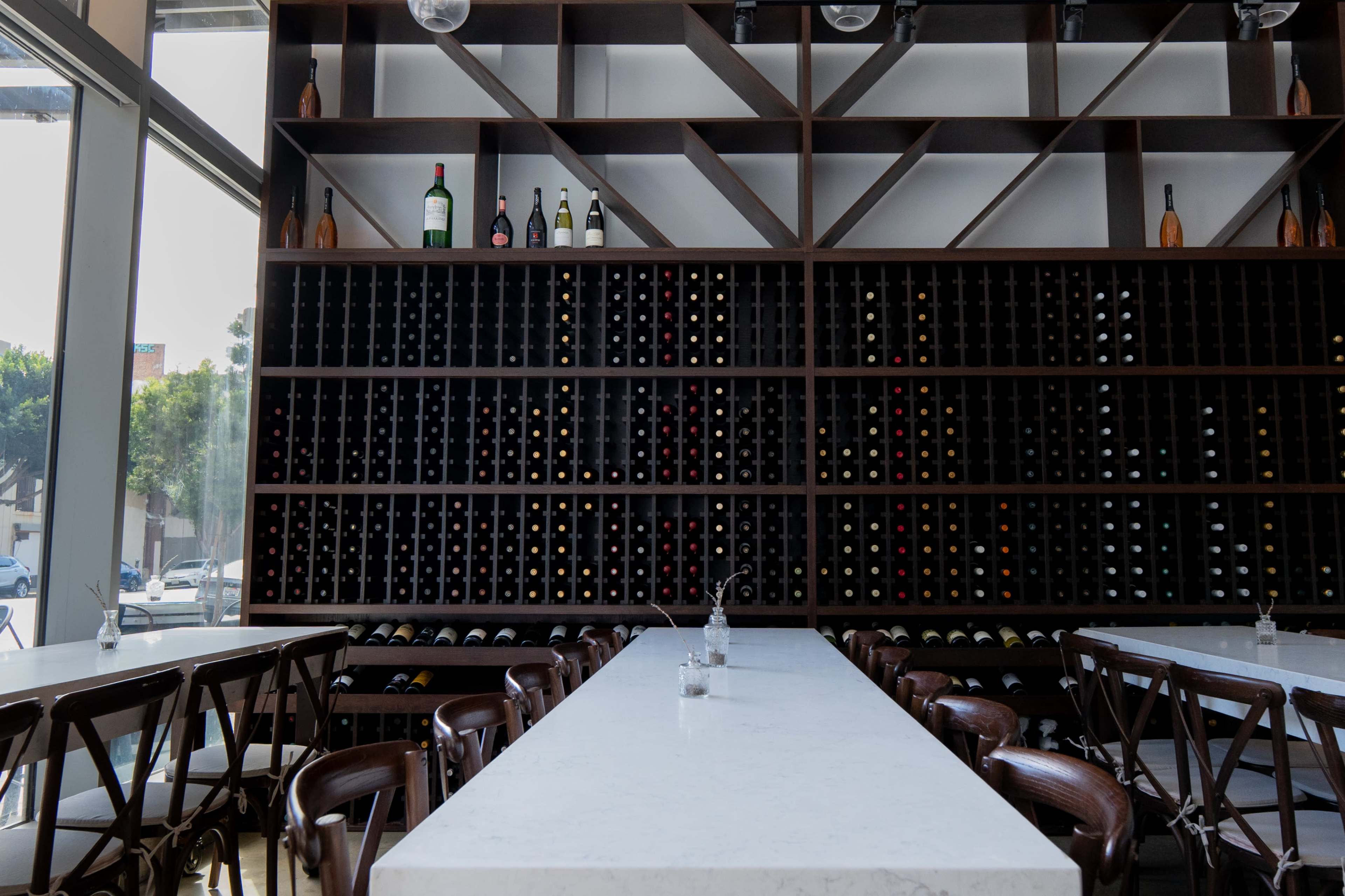 The image features a modern restaurant interior with a long marble table and a wine rack displaying numerous bottles arranged against a dark wooden wall.